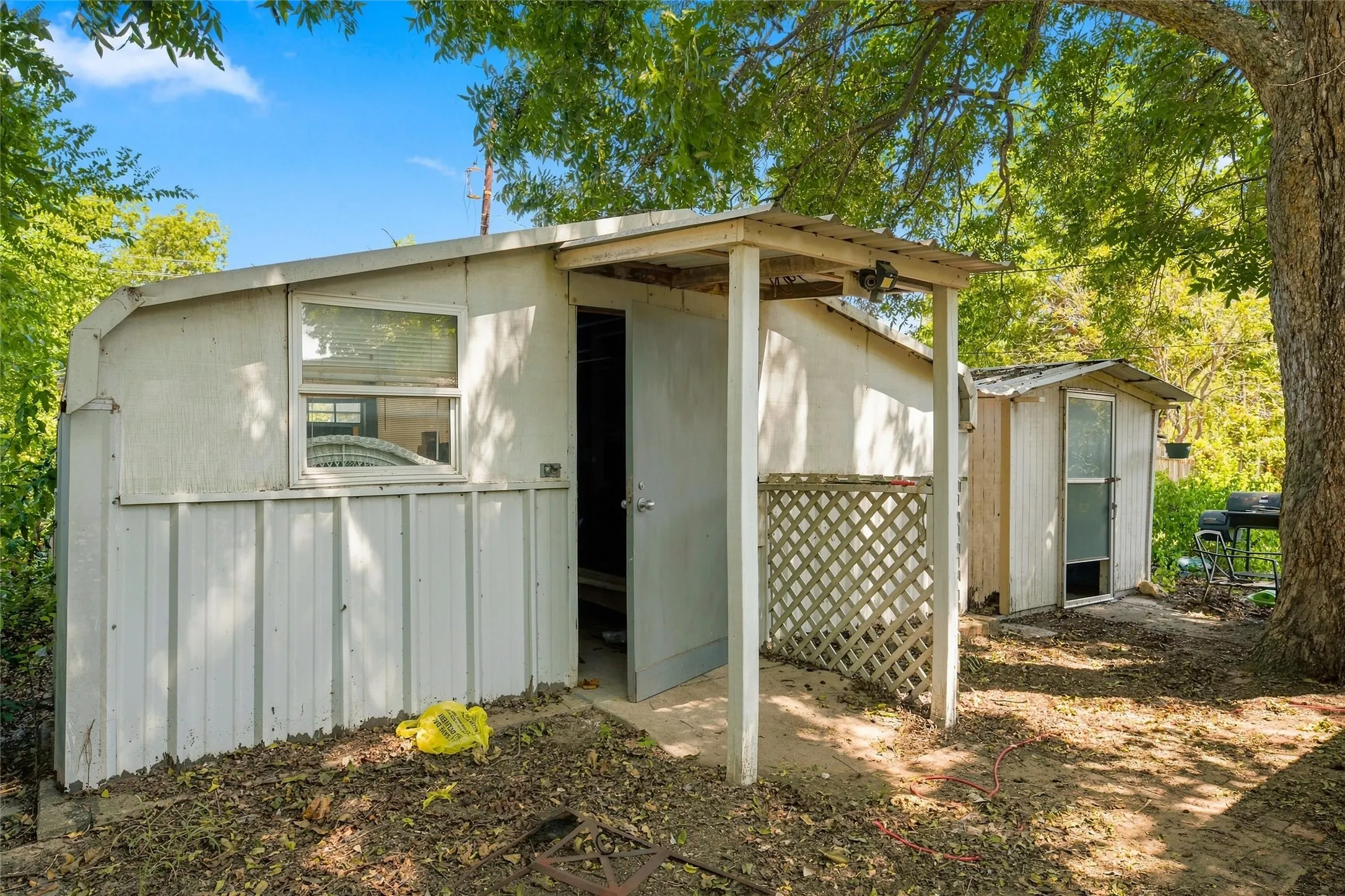 Charming cottage-style residence featuring a covered front porch with lattice detailing, metal corrugated siding exterior, and large front-facing window