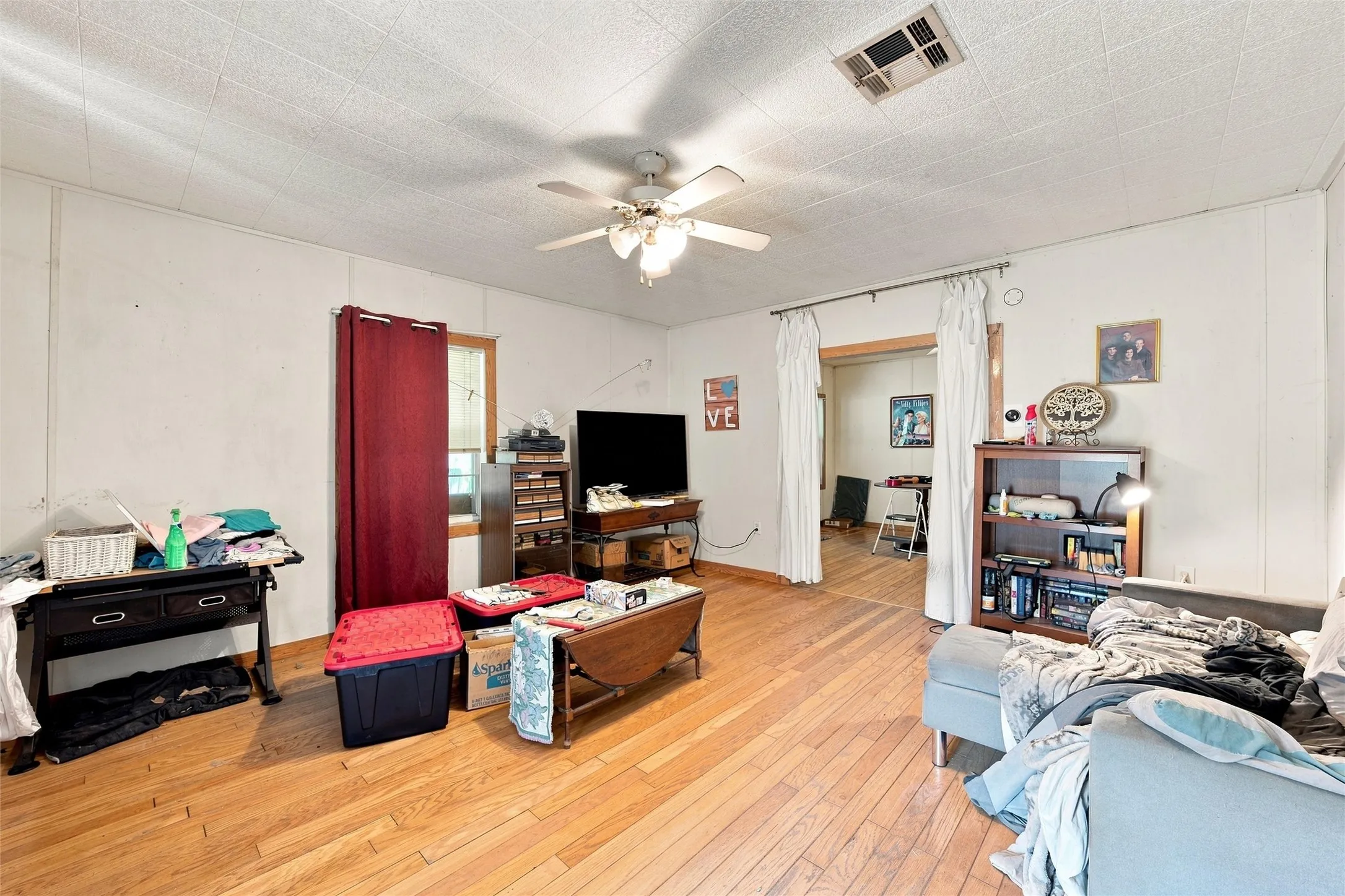 Spacious room featuring wood-finish flooring, white paneling, and a ceiling fan