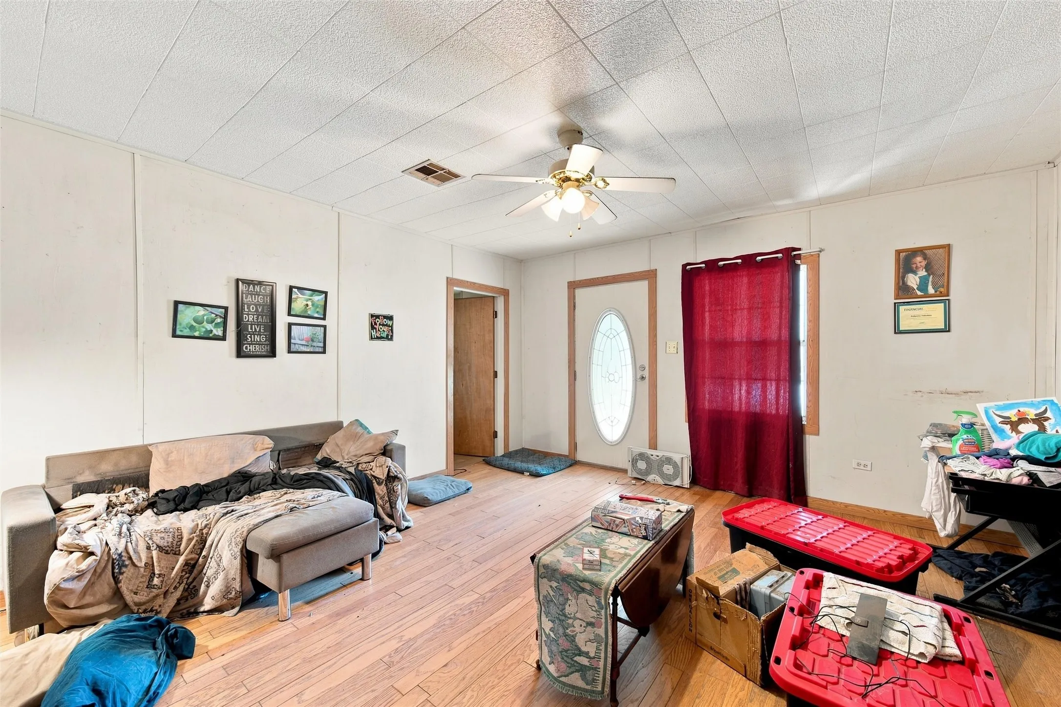 Spacious room with wood-finish flooring, ceiling fan with integrated lighting, and multiple entry points including a solid wood door and arched doorway