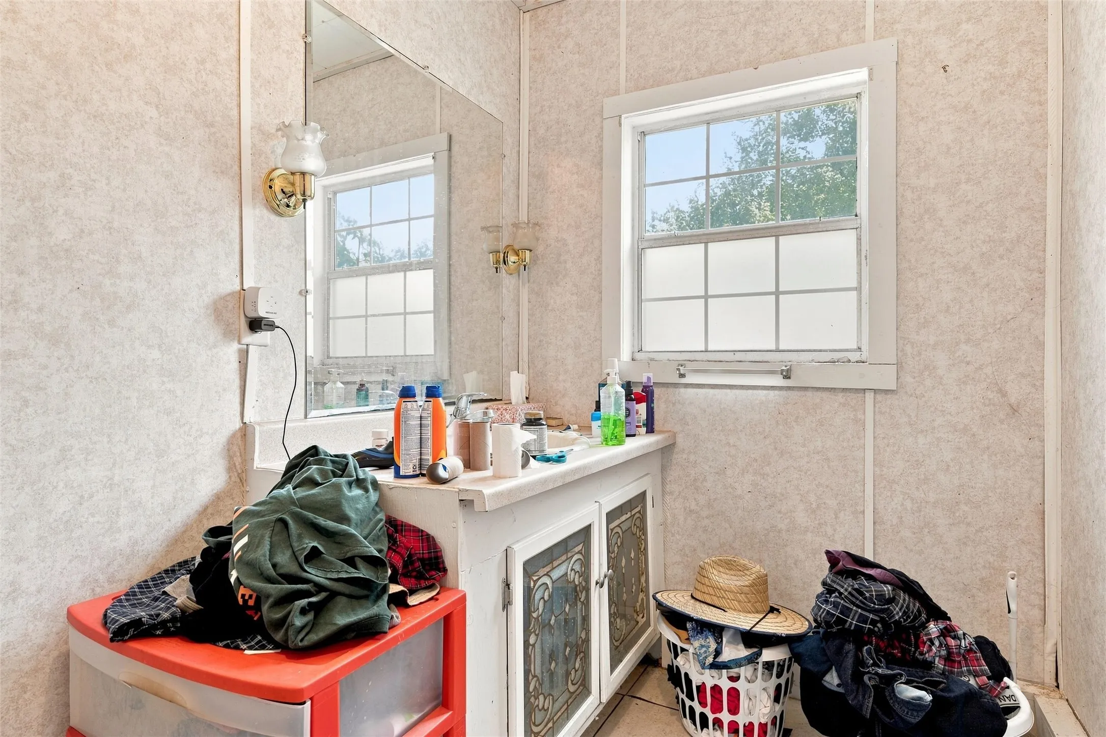 Bathroom featuring a window with grid panes, a vanity with cabinet storage, a wall-mounted mirror, and decorative wall sconce lighting