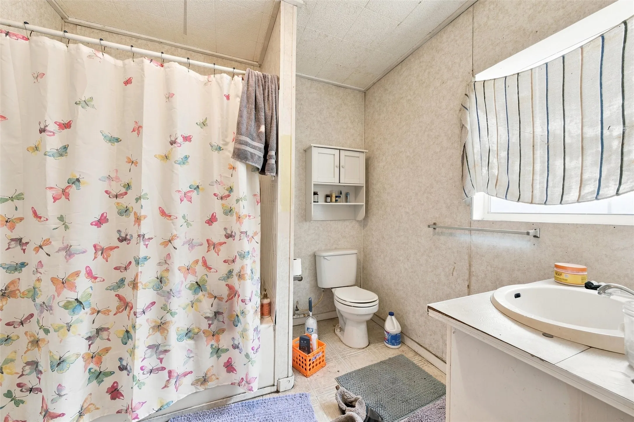 Bright and functional bathroom featuring a floral-patterned shower curtain, white porcelain fixtures, and a ceramic sink with chrome hardware