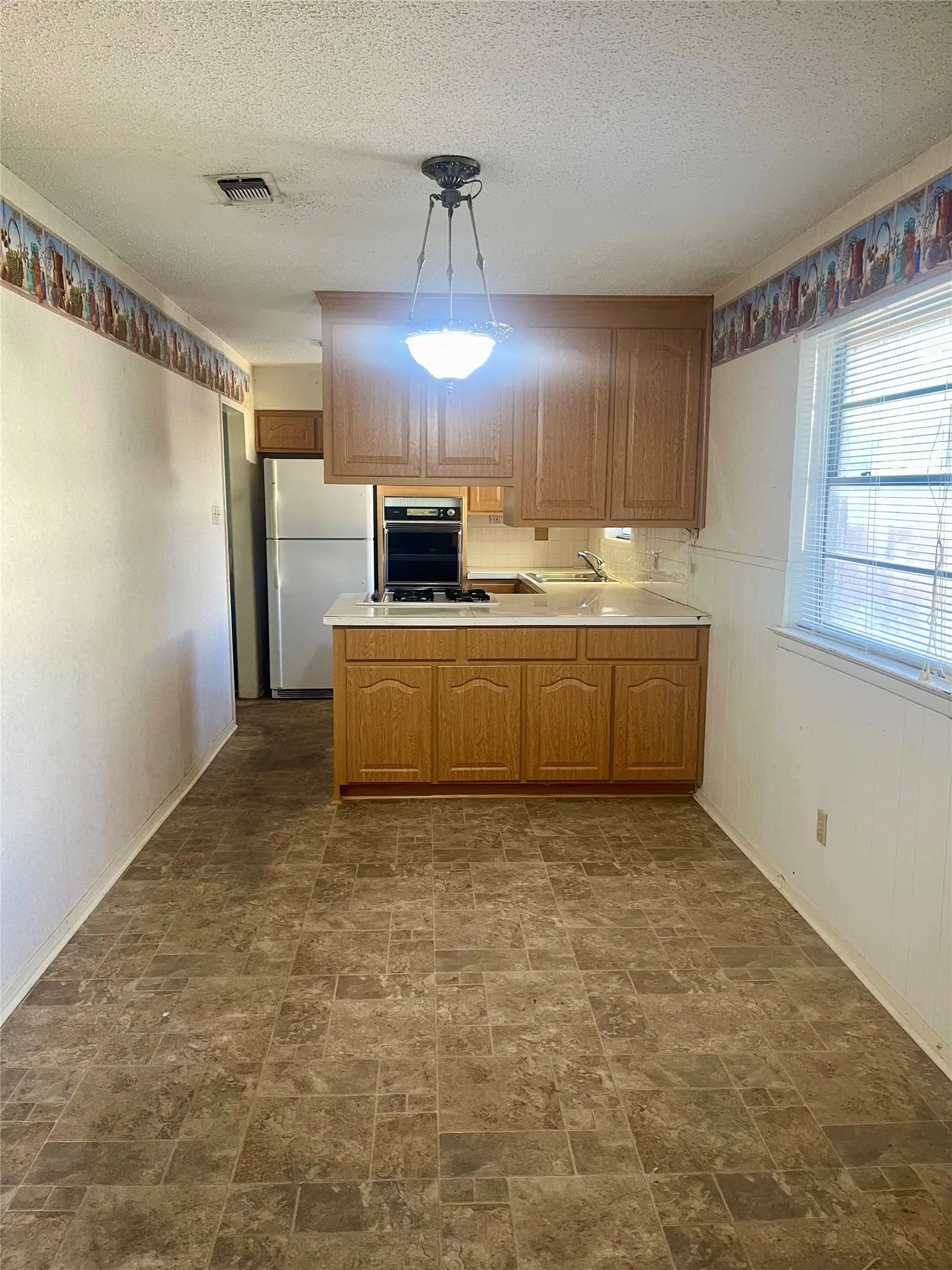 Spacious kitchen featuring wood-finish cabinetry, laminate countertops, stainless steel appliances, and a central island with additional workspace