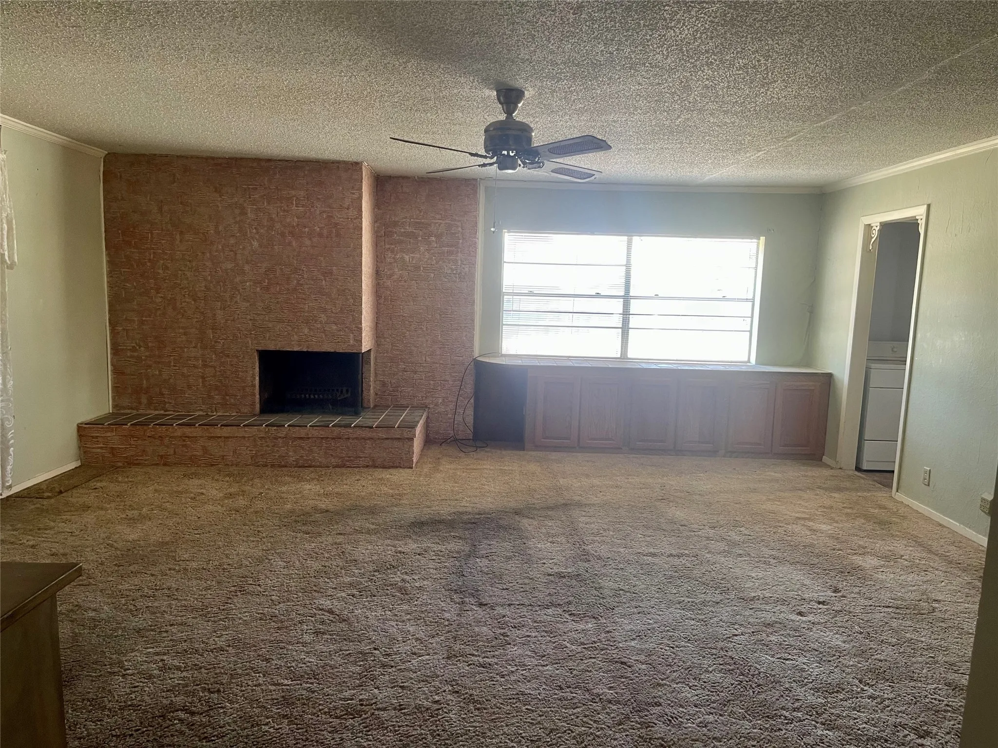 Spacious living area featuring a brick fireplace with a raised hearth, a ceiling fan, and built-in cabinetry beneath large windows