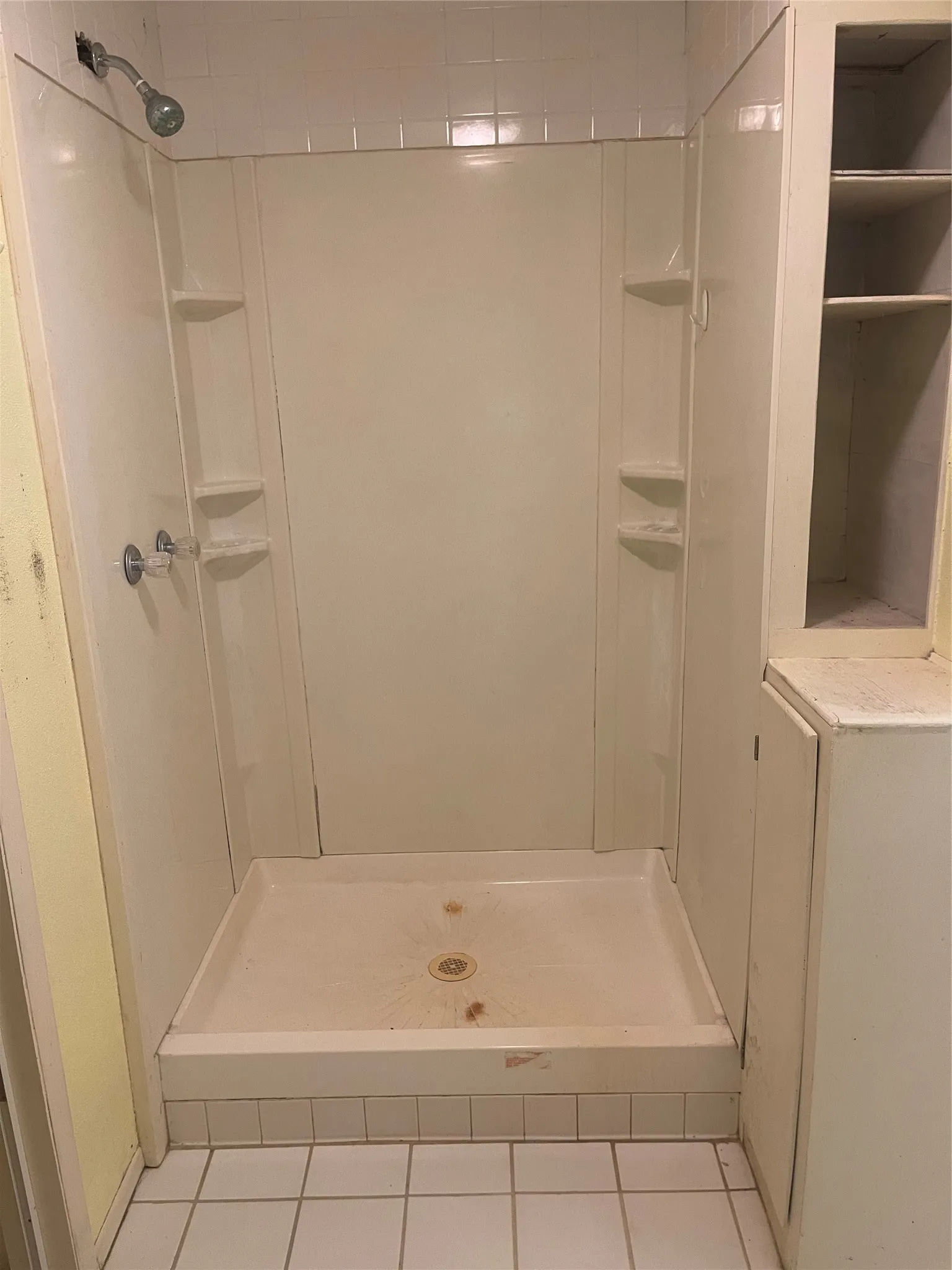Spacious shower enclosure featuring seamless fiberglass surround with integrated shelving, chrome showerhead, and pressure-balance valve