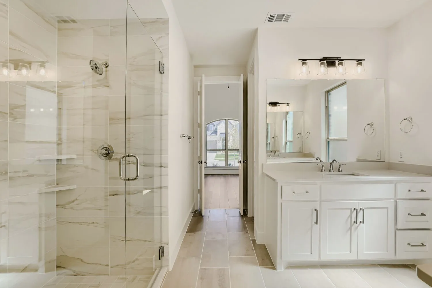 Glass-enclosed shower with tiled walls and built-in shelving, wood-finish tile flooring, single vanity with white cabinetry, rectangular mirror, and a wall-mounted light fixture