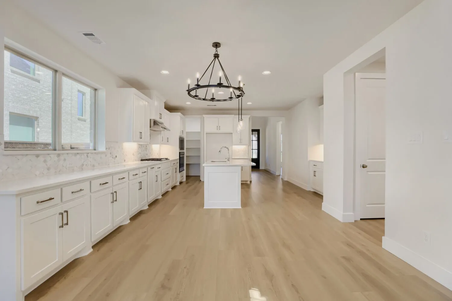 Kitchen featuring light wood-finish flooring, white cabinetry, a central island with a sink, and a black chandelier