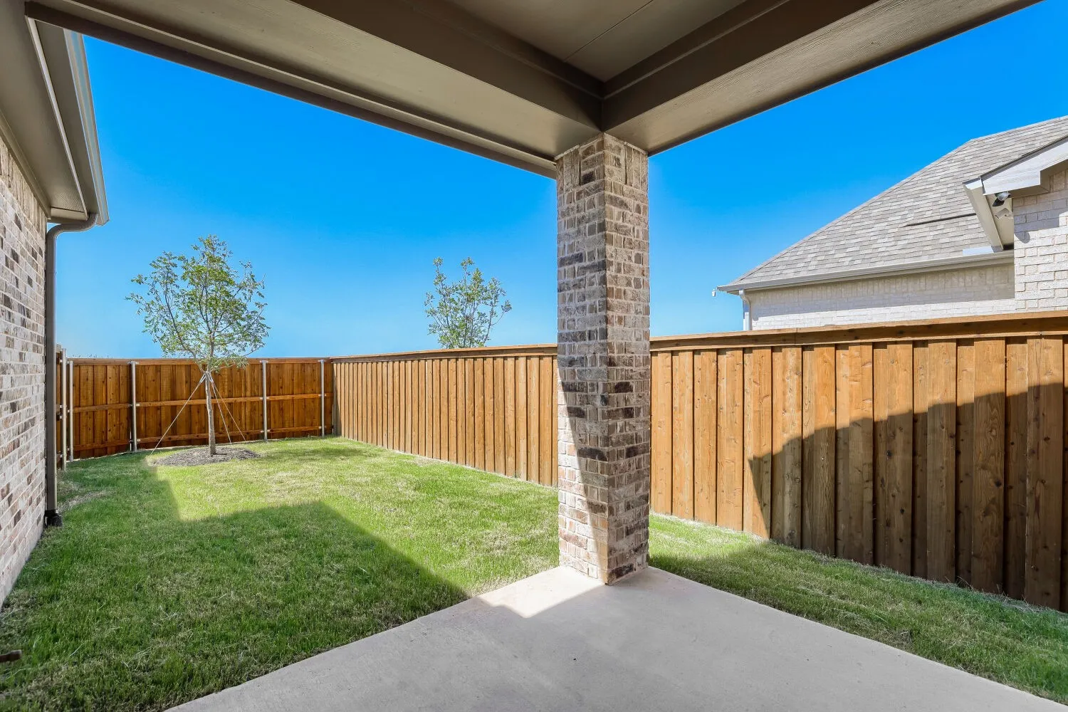 Covered patio with a concrete surface, brick column, and wood plank fencing