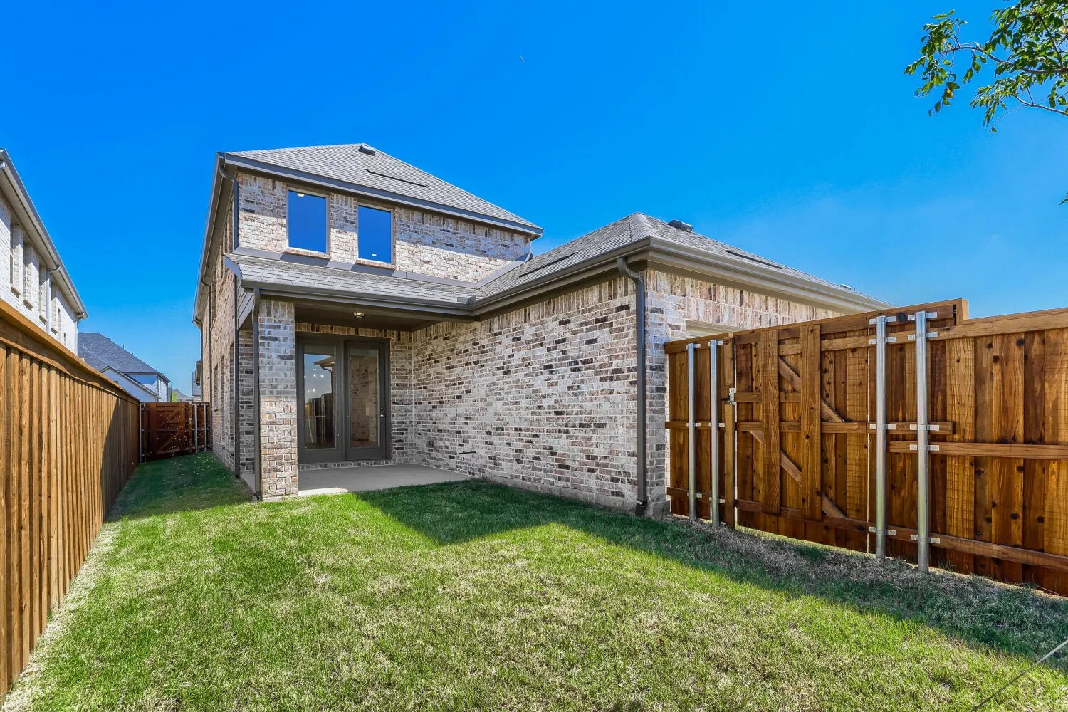 Expansive backyard featuring a manicured lawn, brick exterior, covered patio, and wood privacy fencing