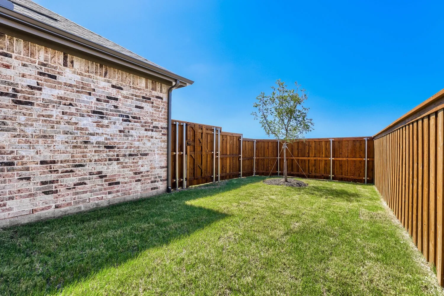 Enclosed backyard featuring manicured lawn, full privacy fencing, and brick exterior