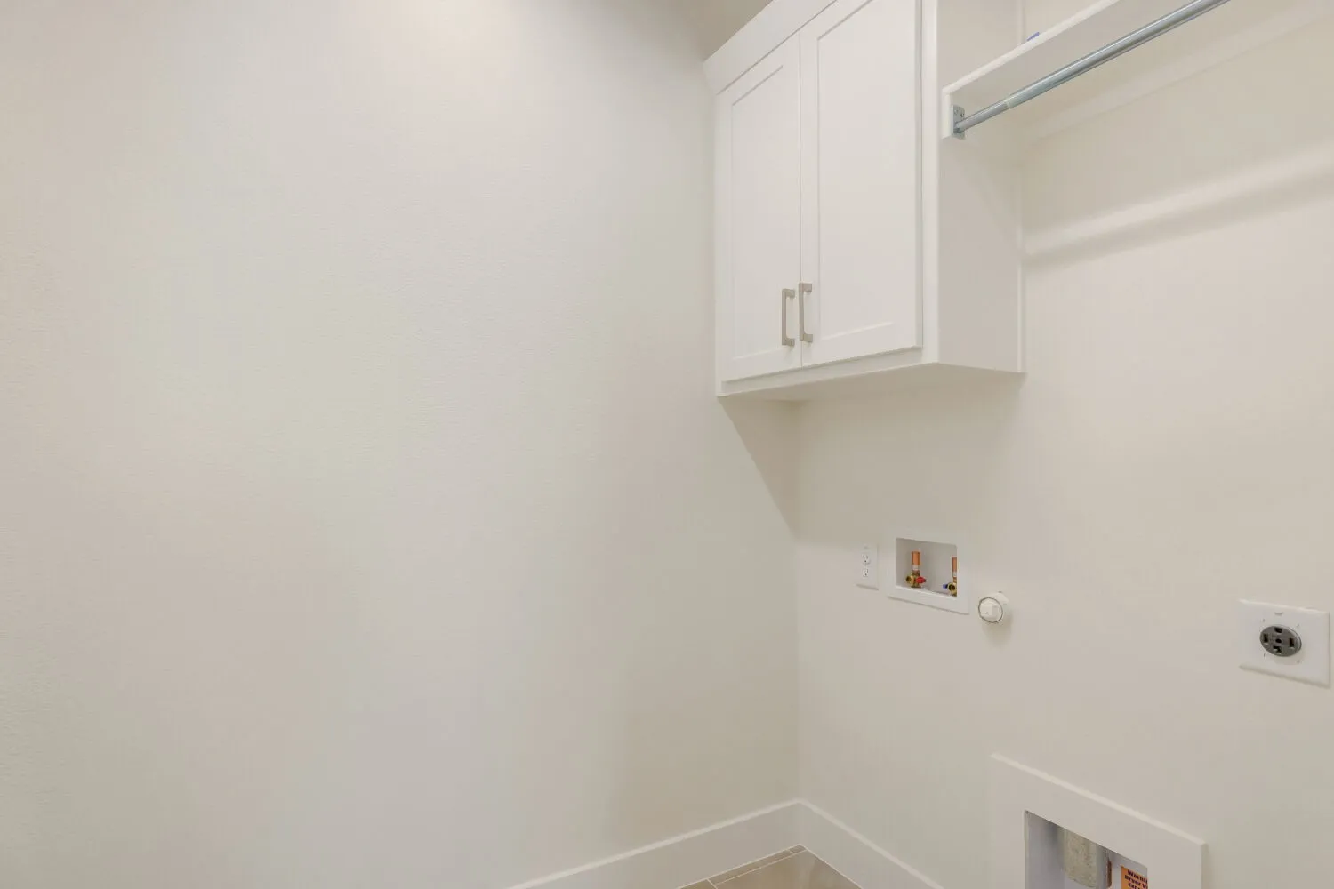 White shaker-style cabinetry, a built-in hanging rod, wall-mounted electrical outlet, and plumbing hookups