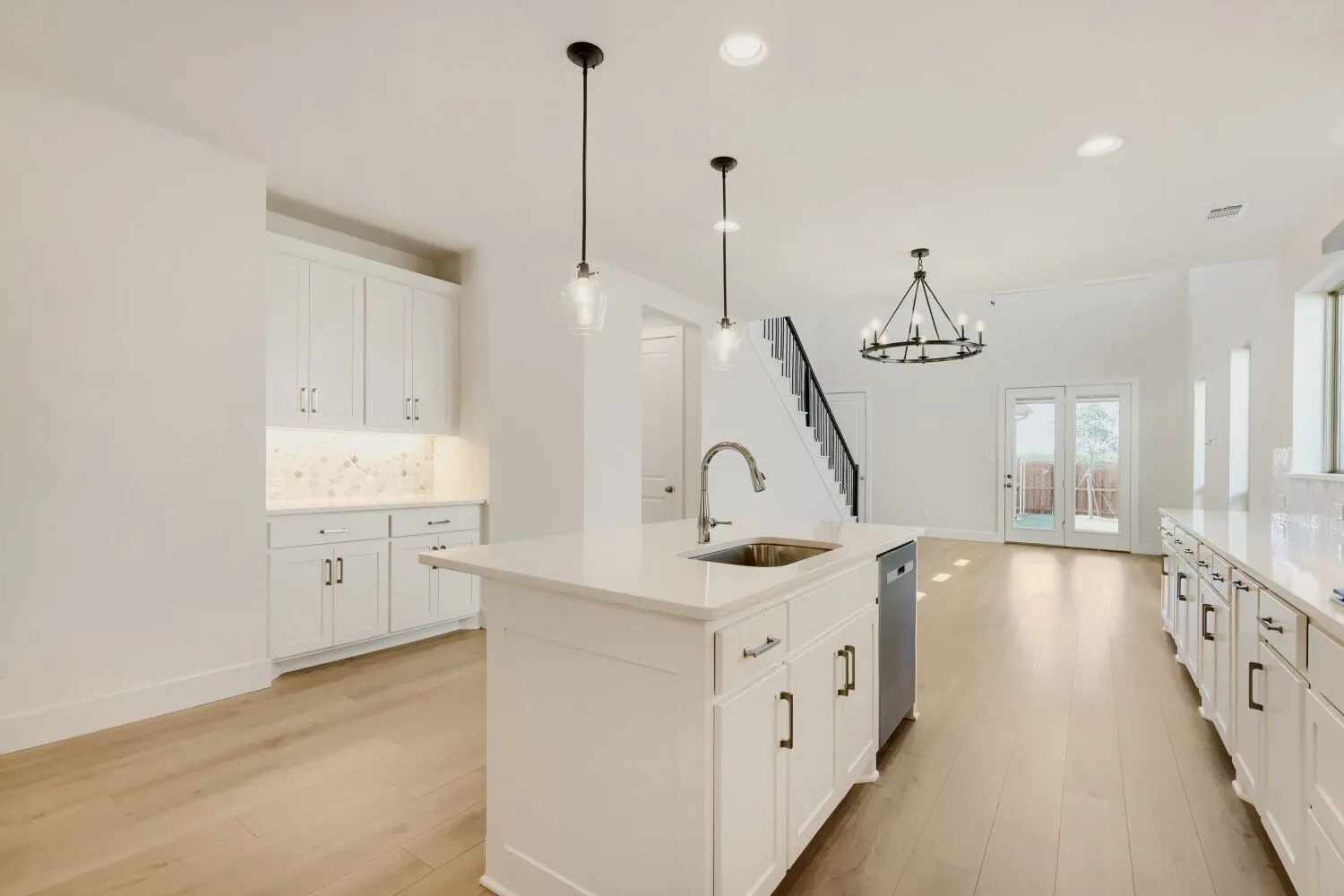 Gourmet kitchen with white cabinetry, stainless steel dishwasher, a central island with sink, and light wood-finish flooring