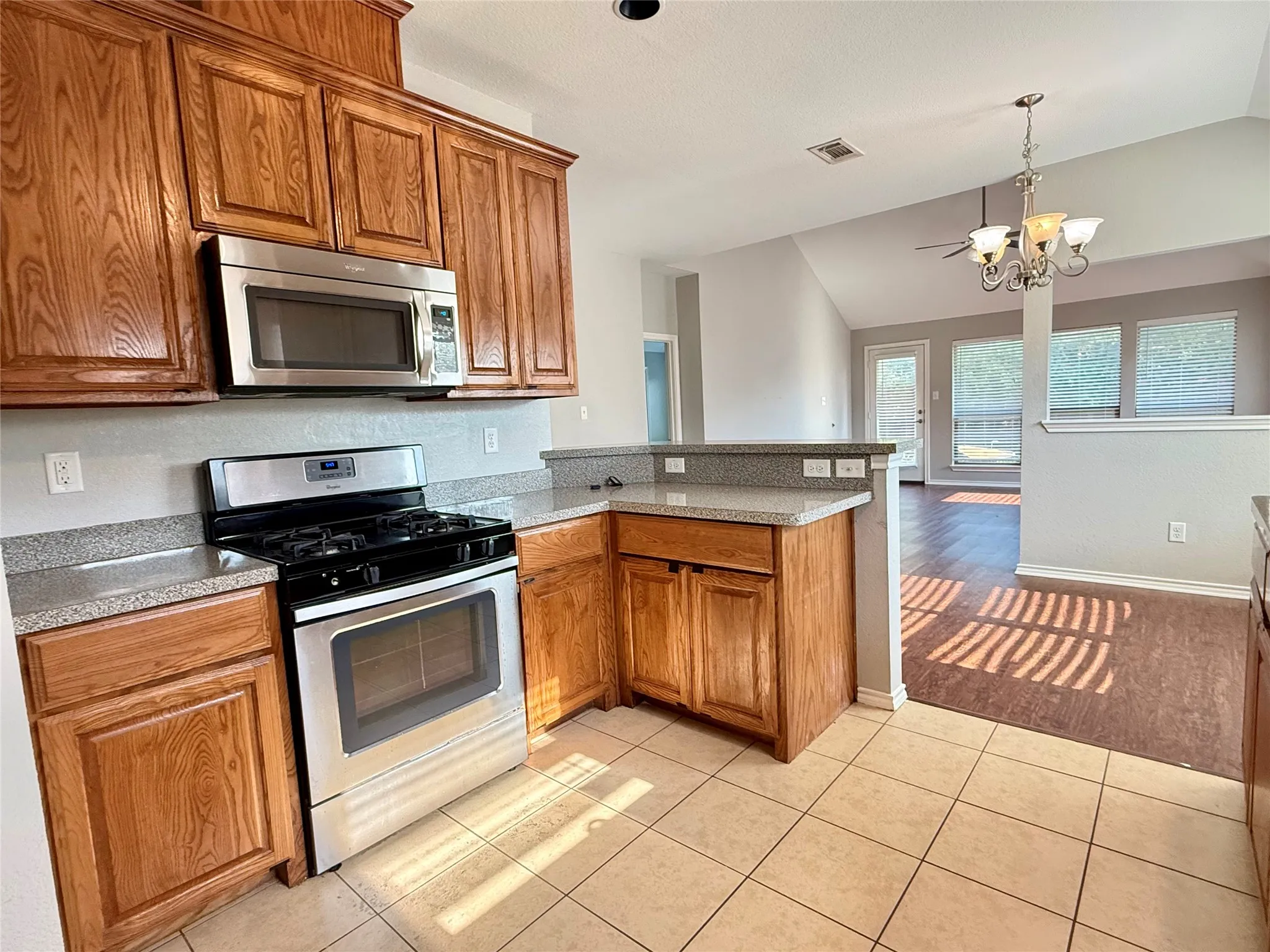 Spacious kitchen featuring warm wood cabinetry, stainless steel appliances including gas range and microwave, granite countertops, and a centered island with additional storage