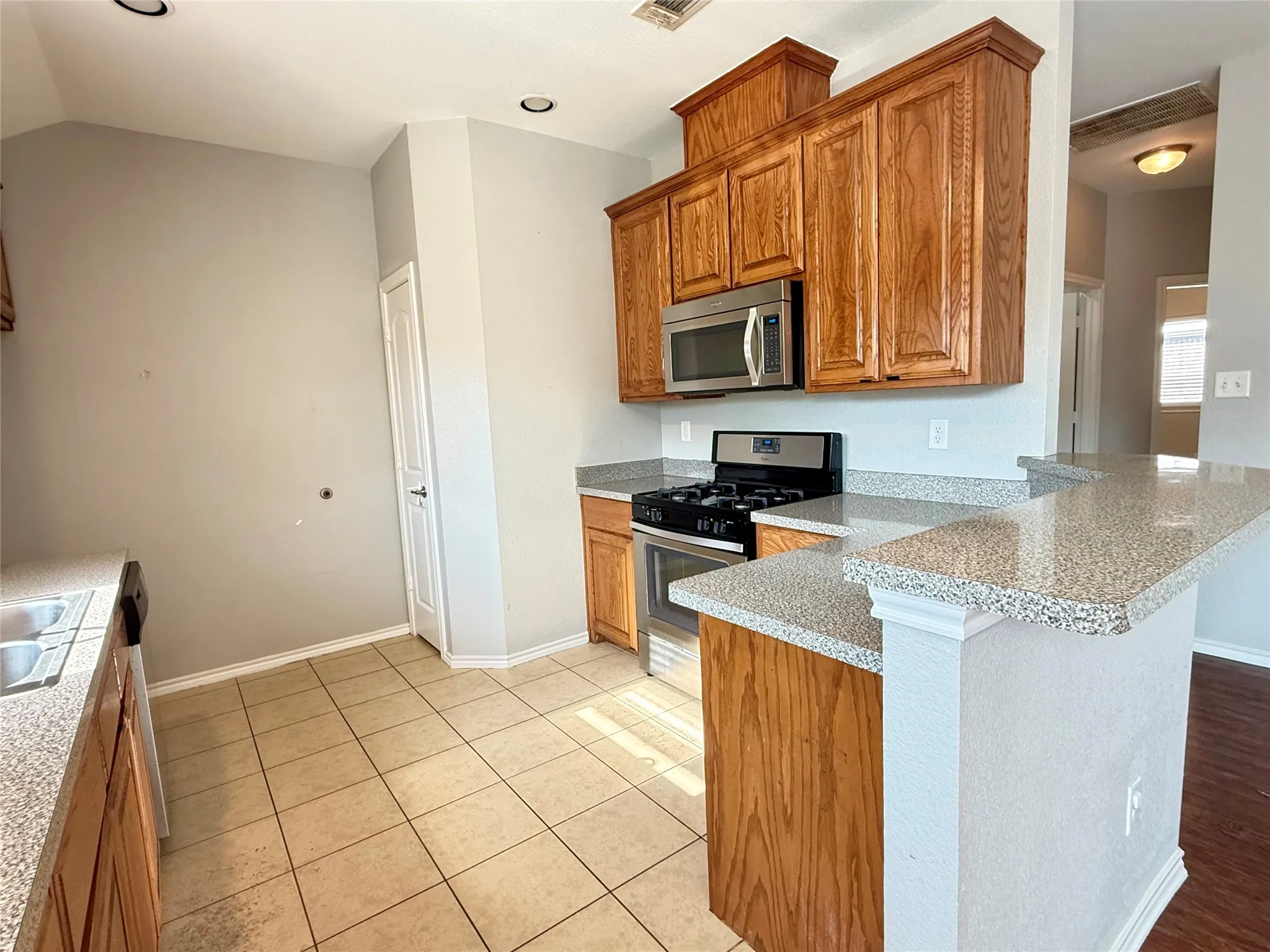Kitchen featuring wood cabinetry, stainless steel appliances, granite-style countertops, and tile flooring