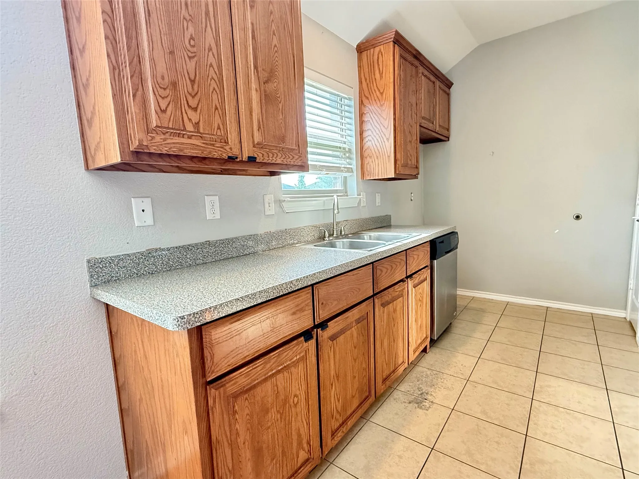 Galley kitchen featuring warm wood cabinetry with raised-panel doors, speckled granite countertops, stainless steel sink with faucet, and ceramic tile flooring