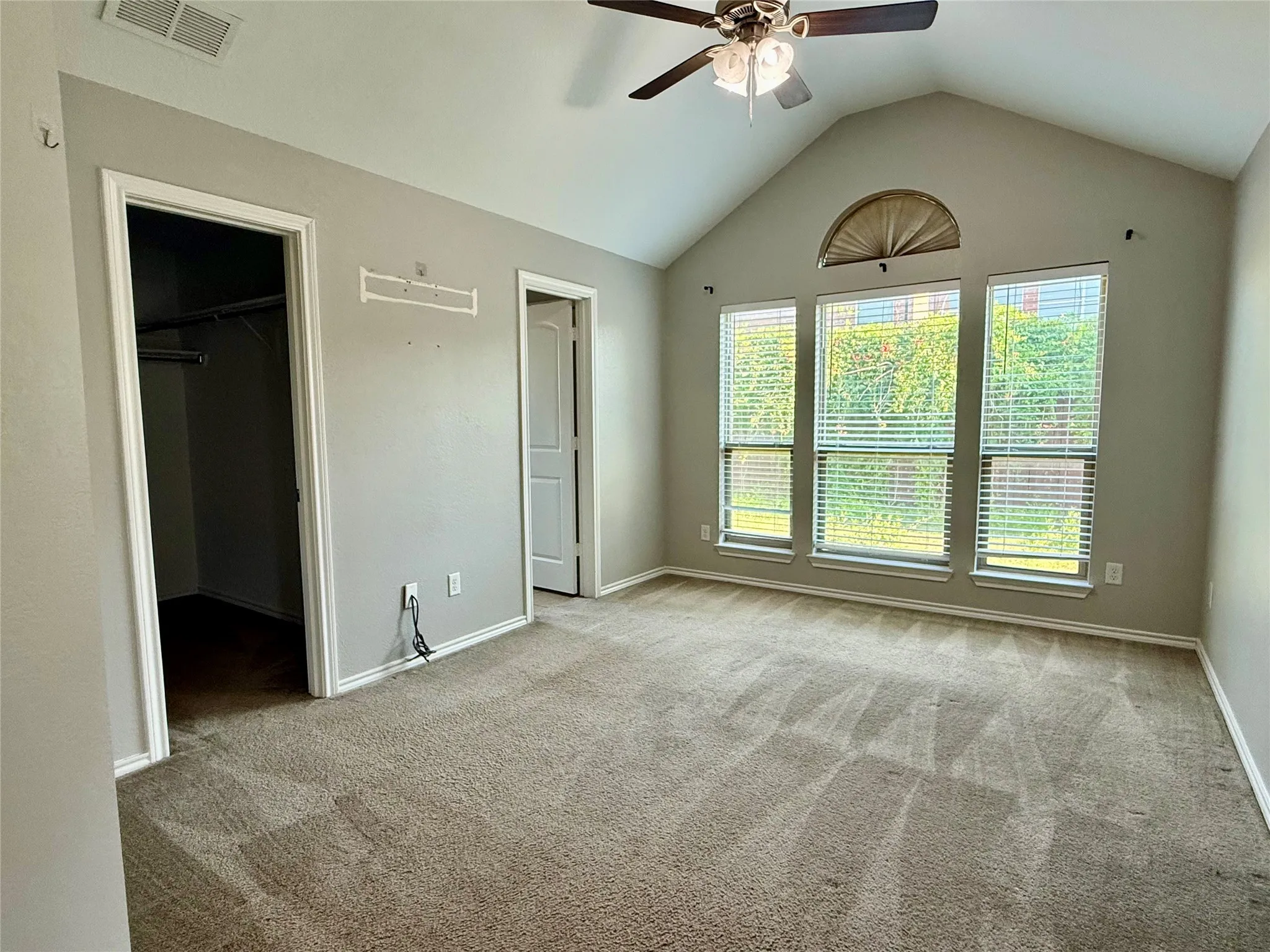 Spacious primary suite featuring vaulted ceilings, ceiling fan with integrated lighting, and abundant natural light from multi-pane glass doors with transom window