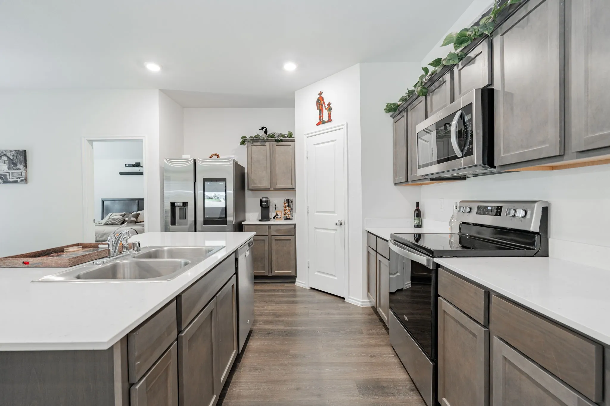 Kitchen with light countertops, dark wood-style flooring, a sink, a kitchen island with sink, and appliances with stainless steel finishes