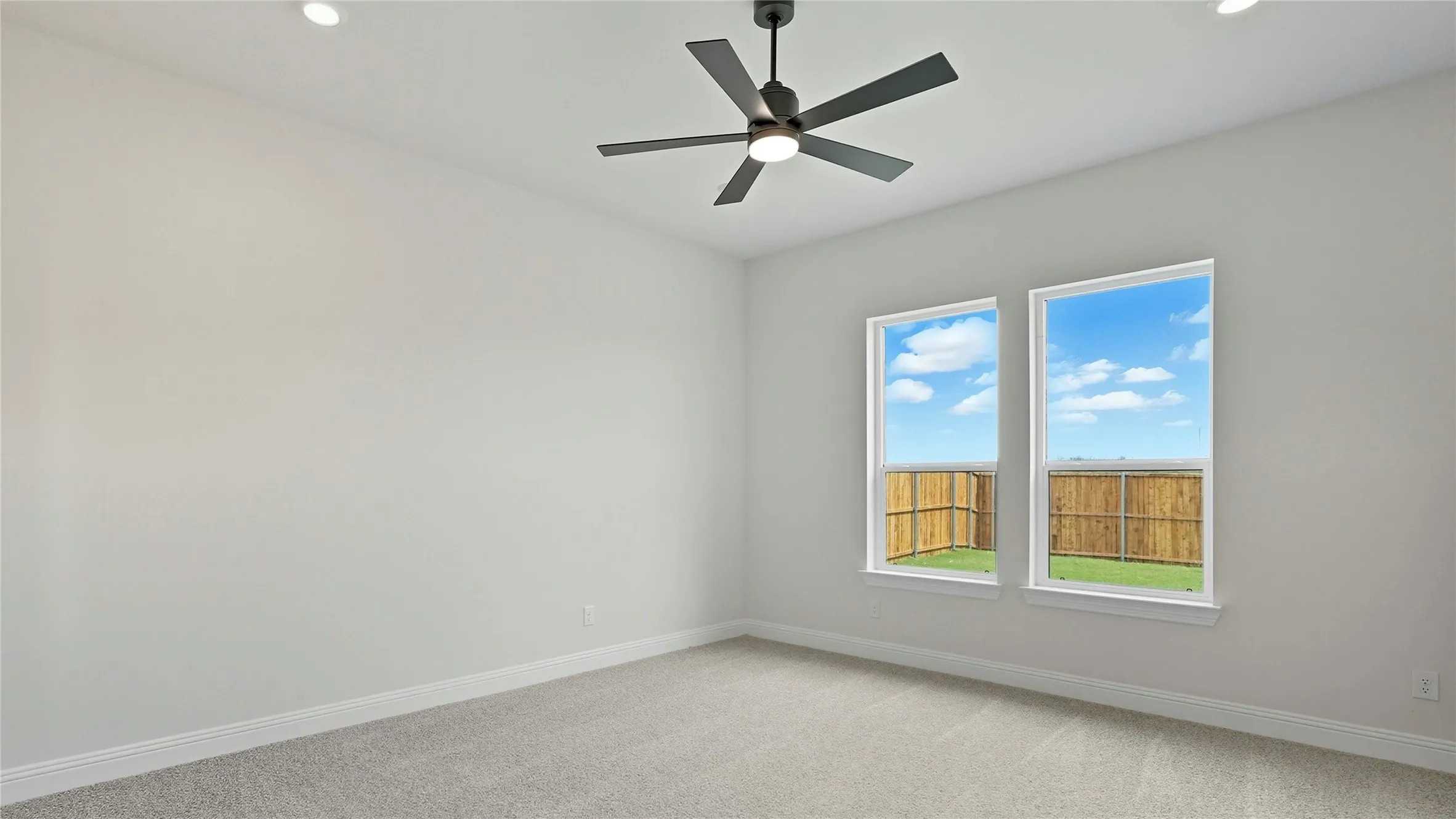 Room featuring twin windows overlooking a fenced yard, a ceiling fan with integrated lighting, recessed ceiling lights, and light-toned carpeting