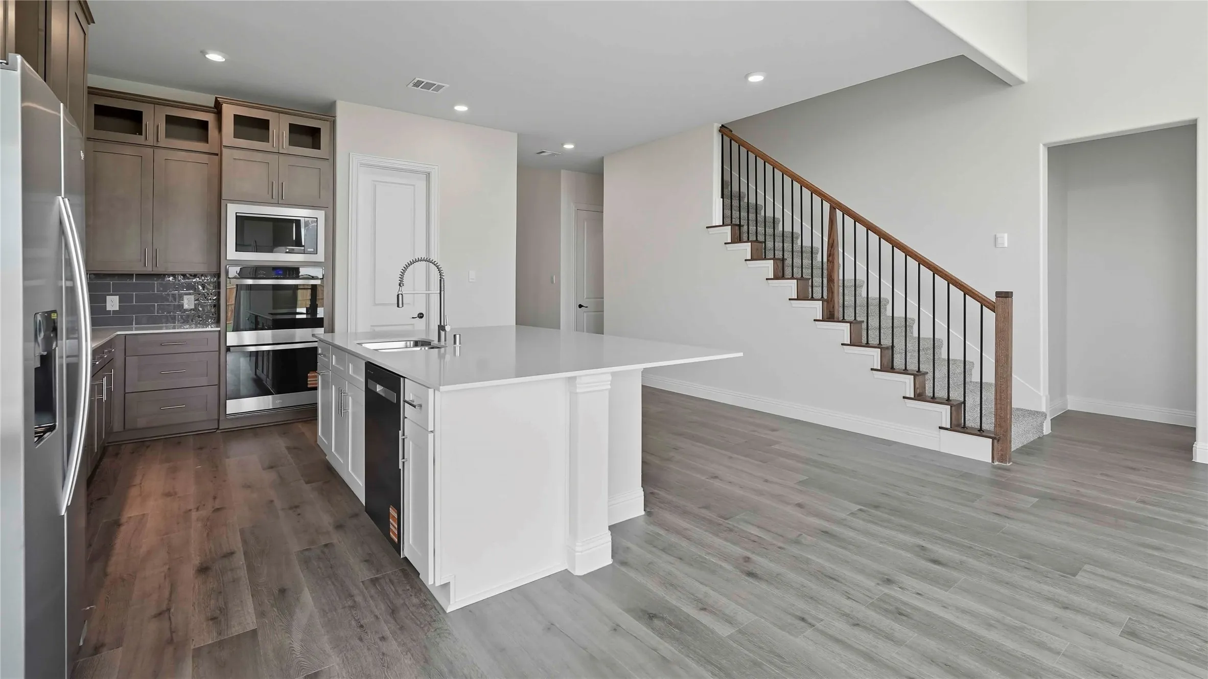 Open-concept kitchen and living space featuring a white quartz island with waterfall edge, stainless steel appliances, white cabinetry, and wood-finish flooring throughout
