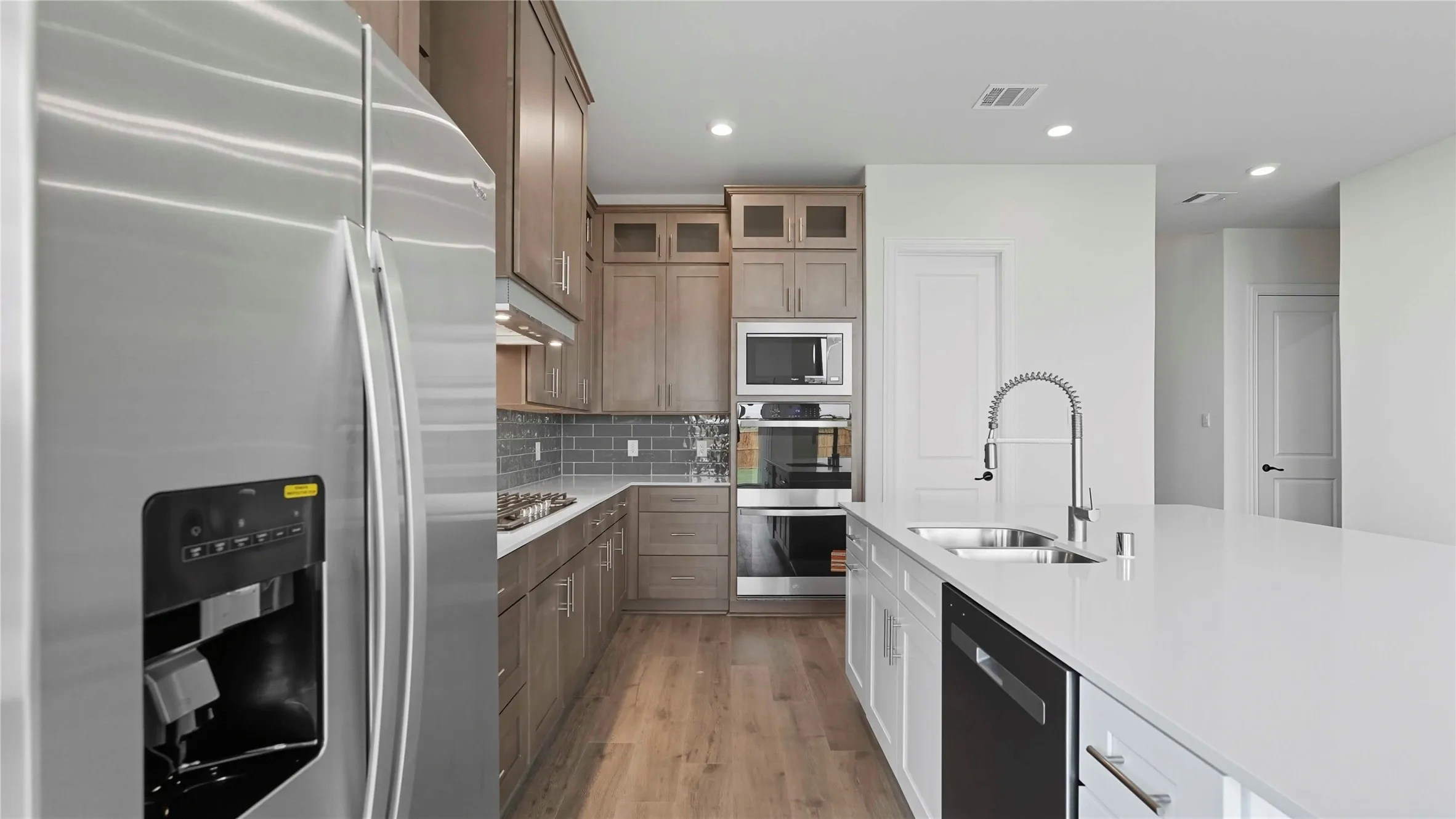 Chef's kitchen featuring white shaker cabinetry, stainless steel appliances including a built-in double oven and ice-maker refrigerator, white quartz countertops, a large island with waterfall edge, wood-finish flooring, and a modern chrome pull-down faucet with gooseneck design
