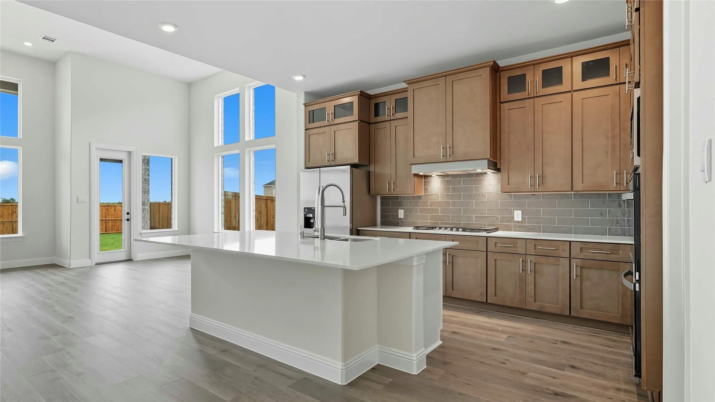 Modern kitchen featuring a central island with a sink, stainless steel appliances, wood-finish flooring, and a tiled backsplash