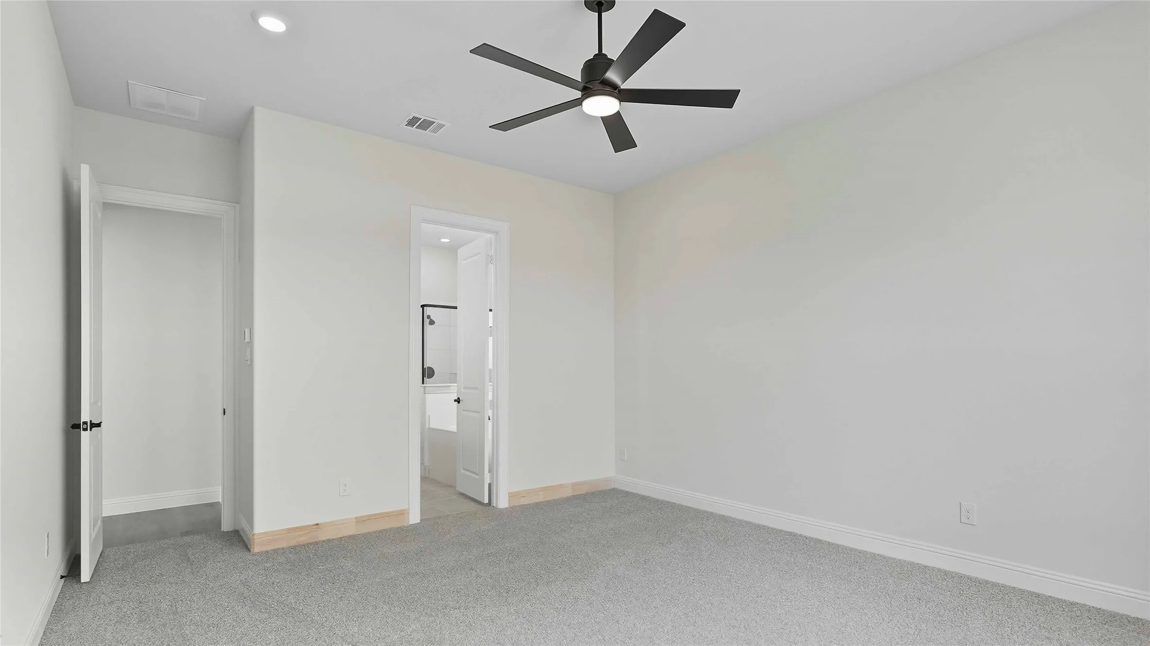 Spacious bedroom featuring neutral wall finishes, recessed ceiling lighting, and a modern ceiling fan with dark metal blades