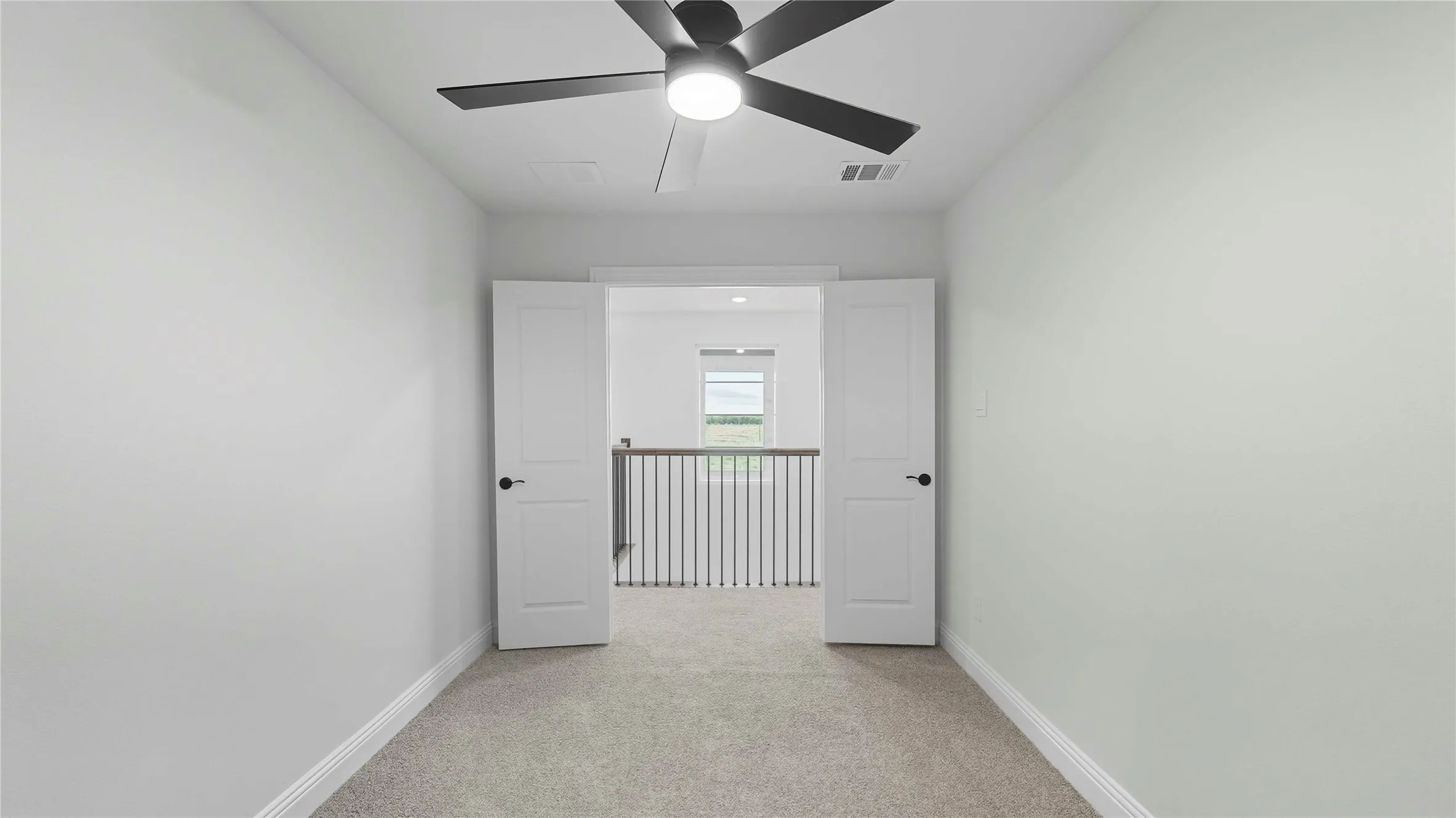 Spacious secondary bedroom featuring neutral carpet flooring, ceiling fan with integrated lighting, and double French doors opening to a gated safety barrier