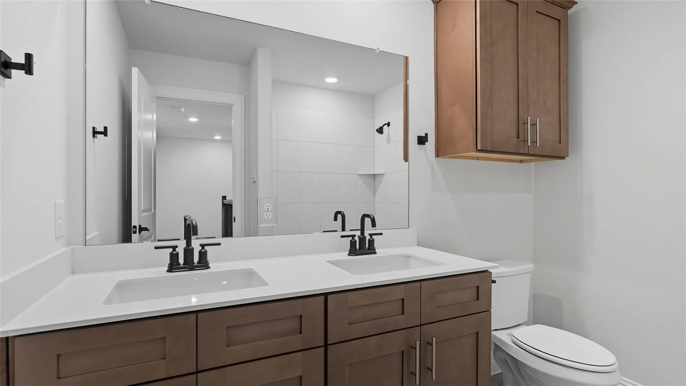 Spa-inspired primary bathroom featuring a dual-sink vanity with wood-finish cabinetry, white quartz countertops, and matte black hardware