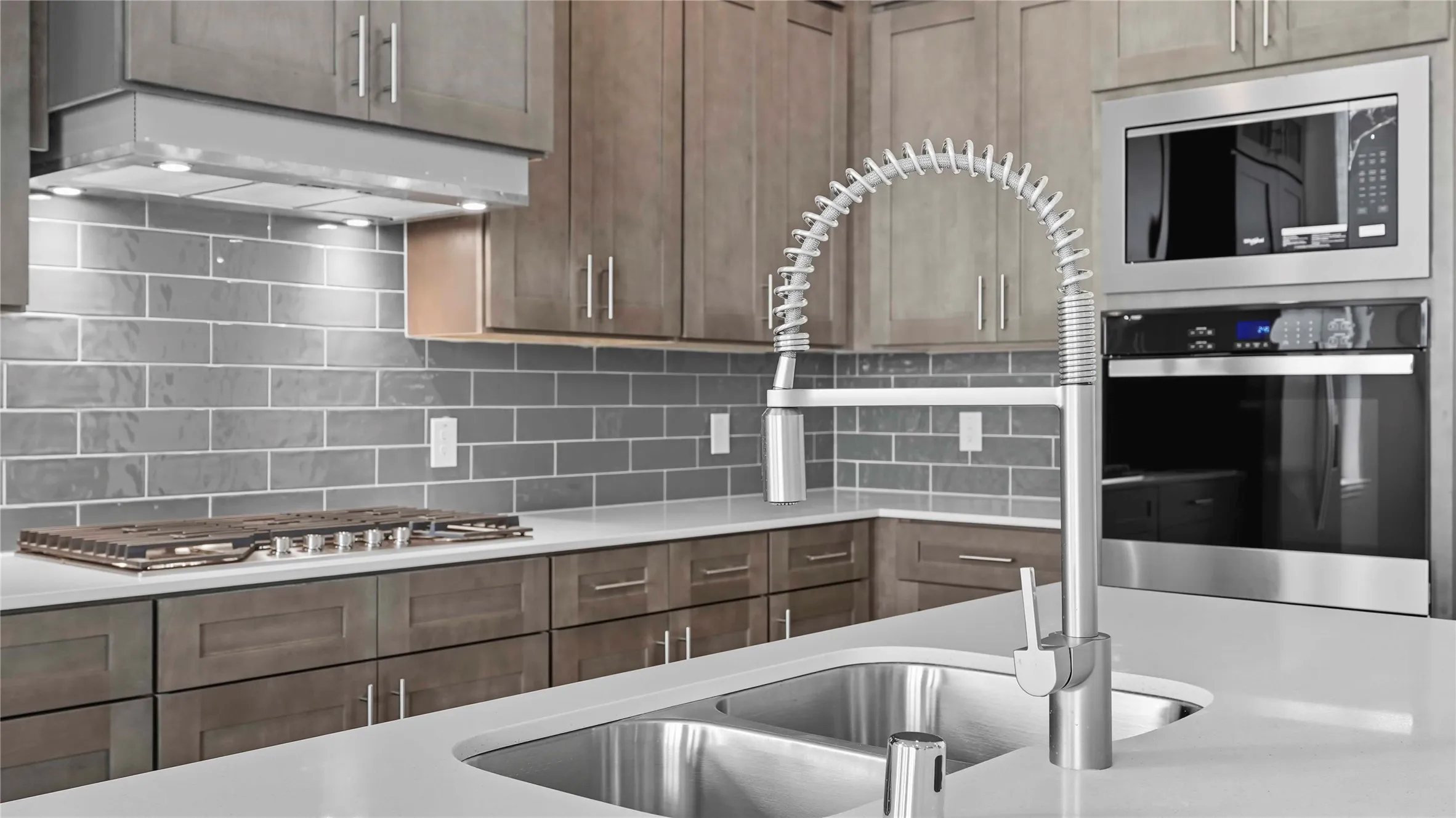 Modern kitchen featuring a double basin stainless steel sink with a high-arch spring faucet, light-toned cabinetry with contemporary hardware, and a gray subway tile backsplash