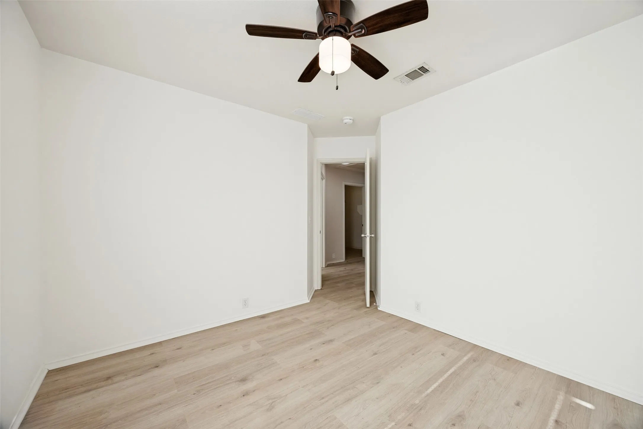 Interior space featuring wood-finish flooring, white walls, and a ceiling fan with integrated lighting