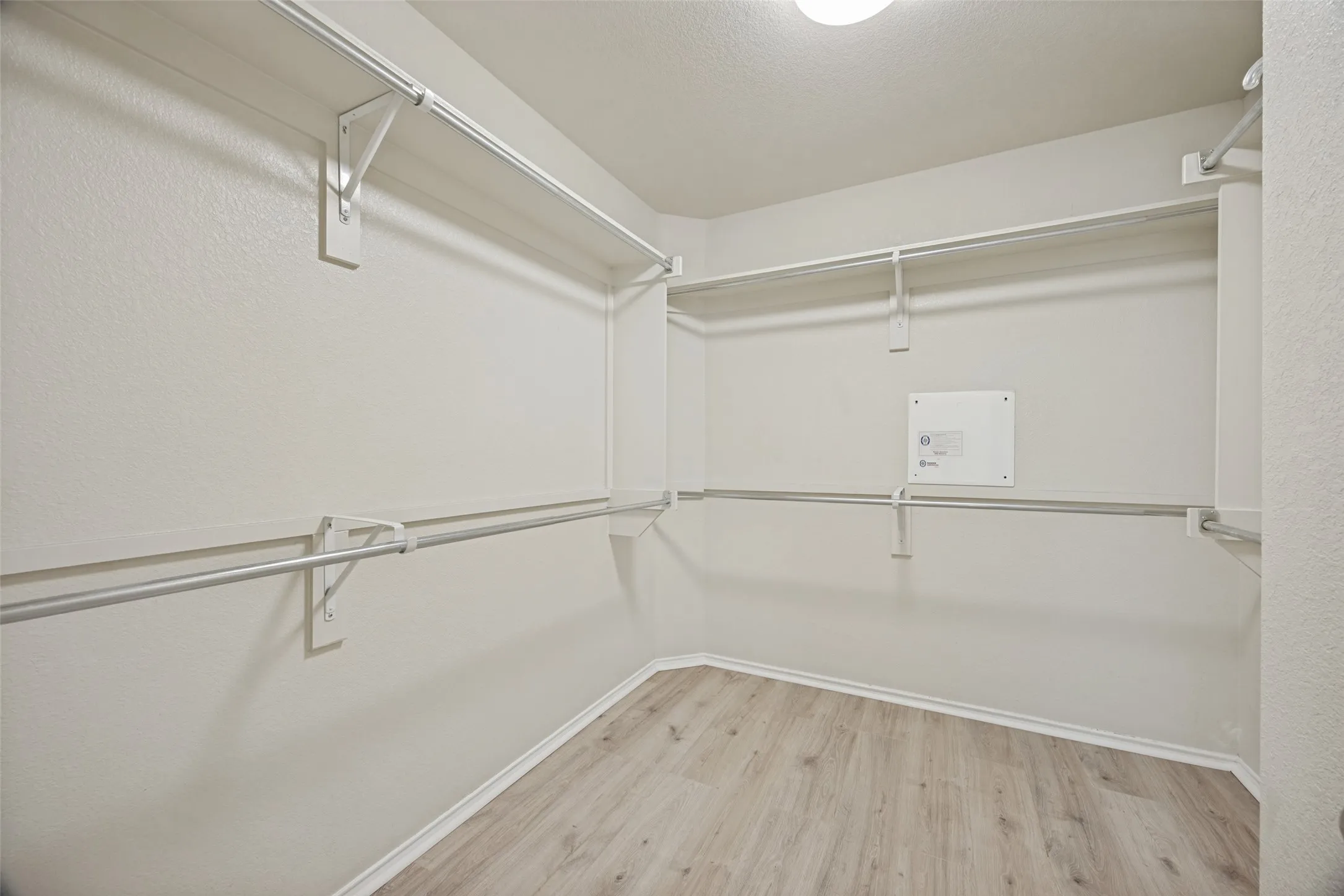 Walk-in closet featuring extensive shelving and hanging rods, wood-finish flooring, white baseboards, and neutral wall paint