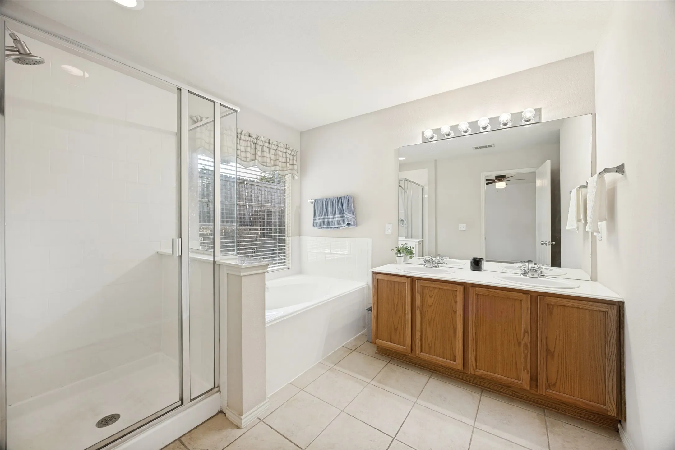 Bathroom featuring a glass-enclosed shower, a large soaking tub, and a dual-sink vanity with wood-finish cabinetry