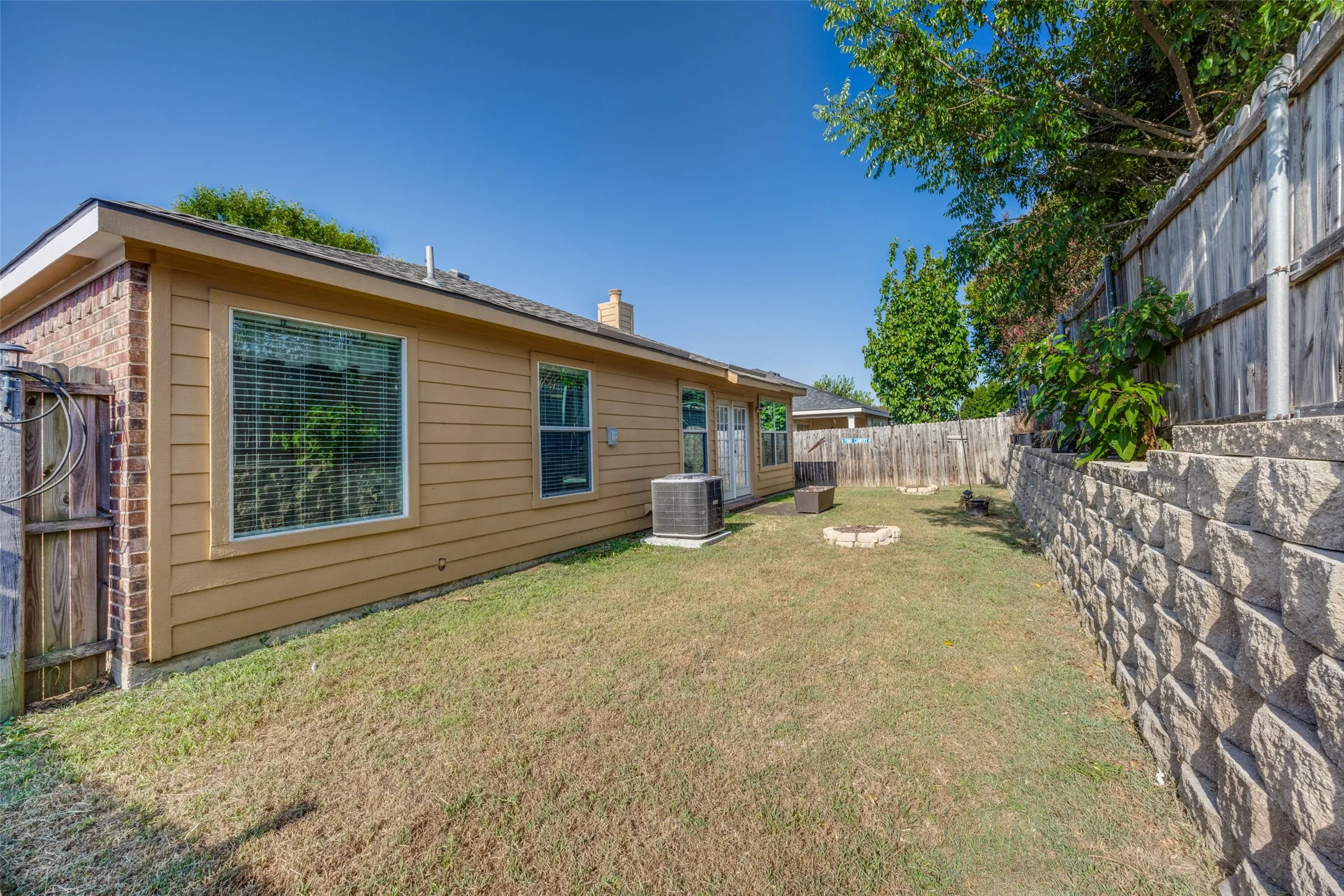 Private backyard featuring a stone retaining wall, wood privacy fencing, and a combination of brick and siding exterior
