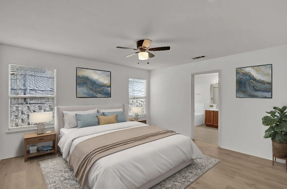 Bright primary bedroom showcasing wood-finish flooring, a ceiling fan with integrated lighting, and large windows allowing natural light throughout