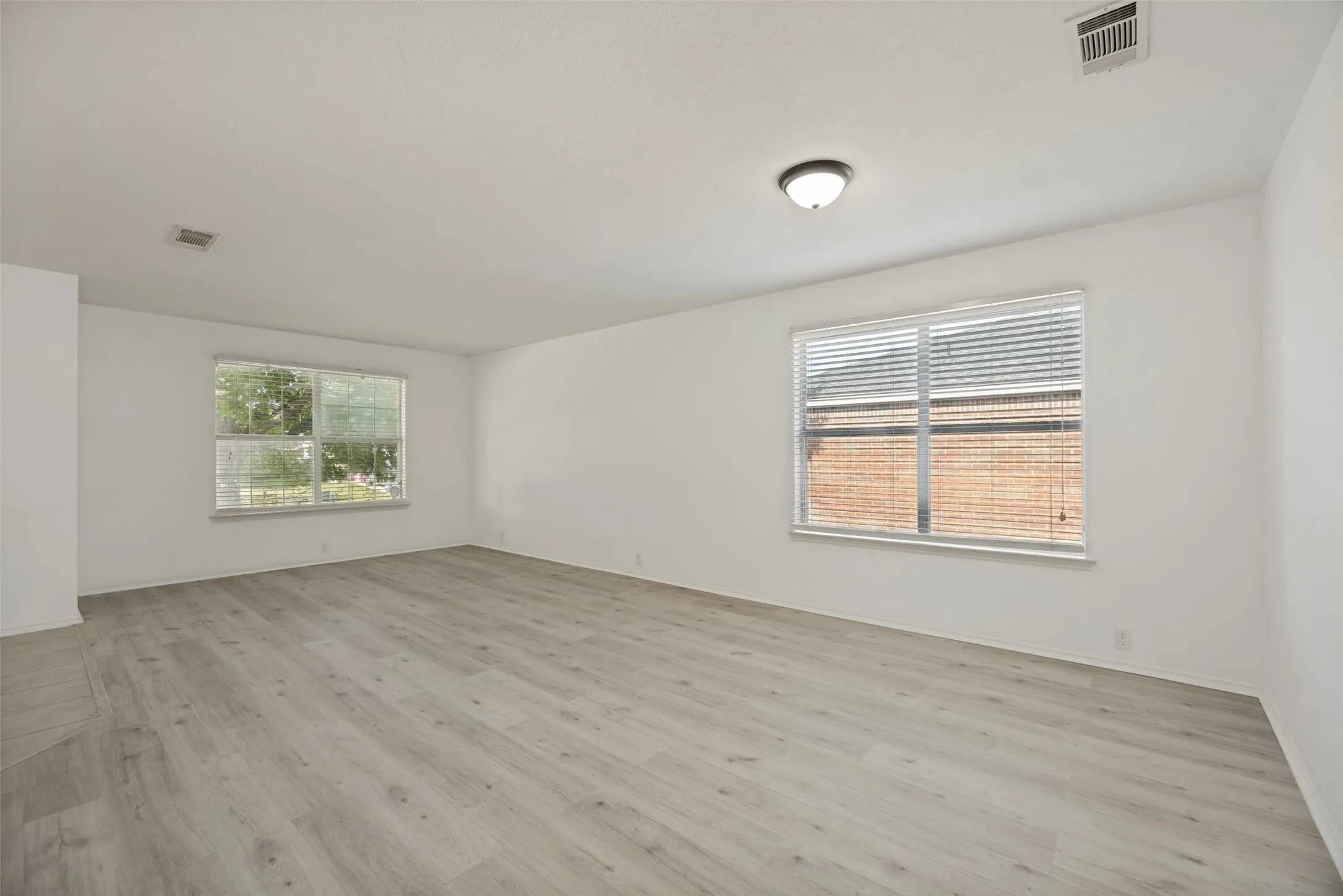 Spacious room featuring light-toned wood-finish flooring, white walls, and two windows with blinds