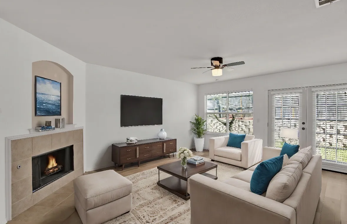 Living area featuring a tiled fireplace with an arched alcove, wood-finish flooring, a ceiling fan with integrated lighting, and multiple windows with blinds
