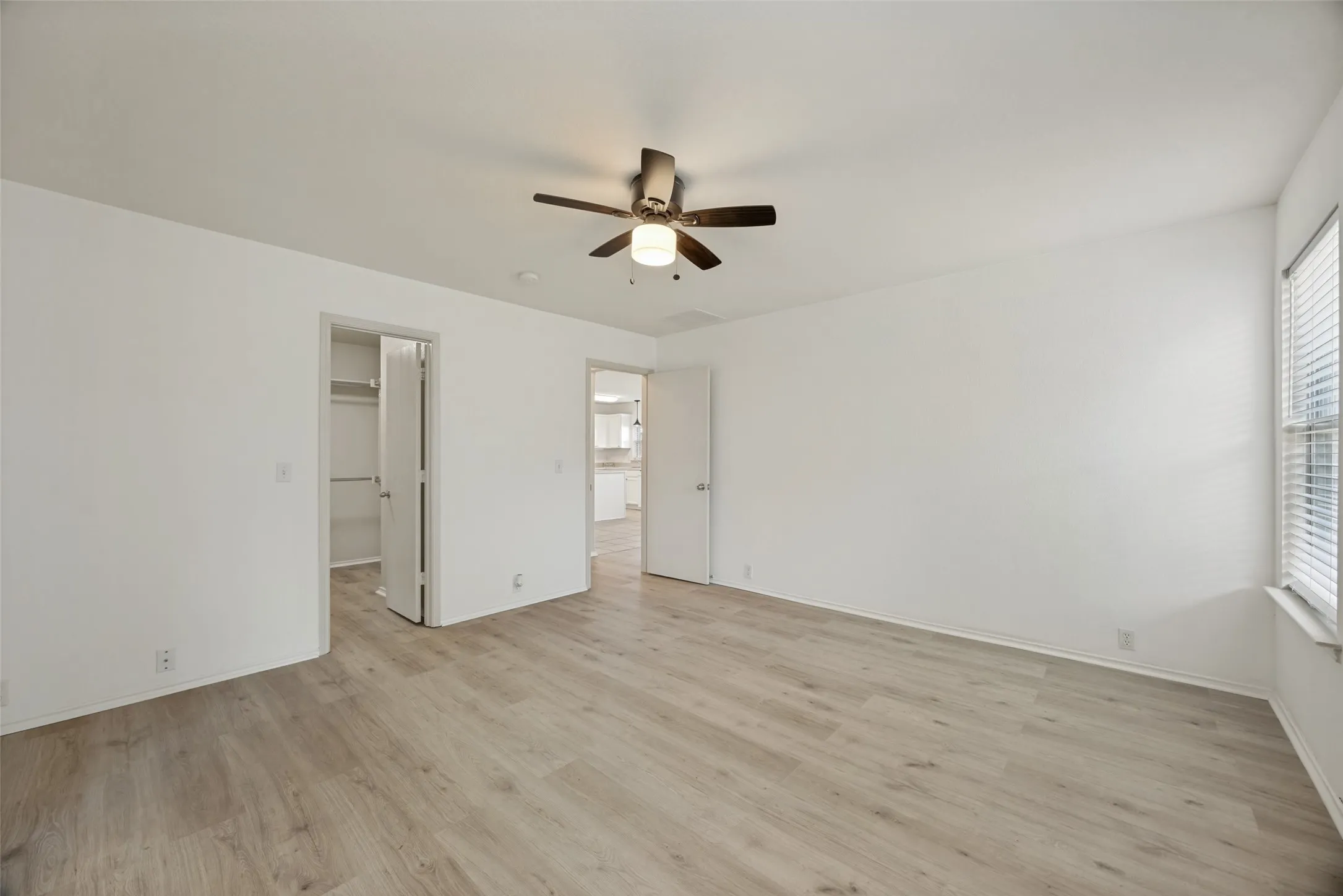 Spacious room featuring wood-finish flooring, white walls, and a ceiling fan with integrated lighting