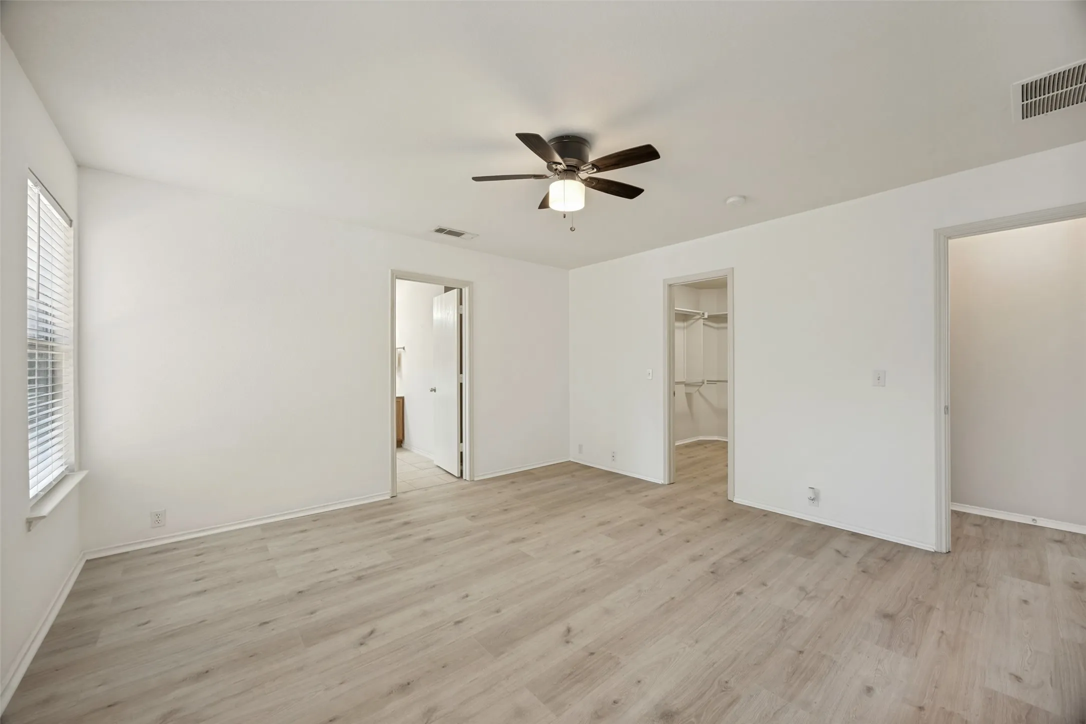 Spacious interior featuring wood-finish flooring, white walls, and a ceiling fan with integrated lighting