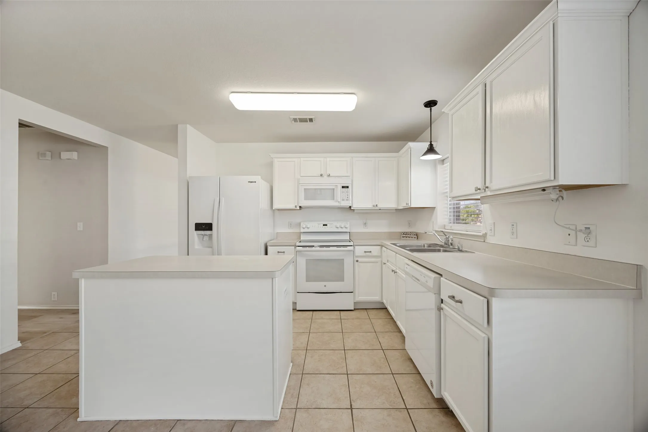 Kitchen featuring white cabinetry, light-toned countertops, a central island, tile flooring, and integrated white appliances