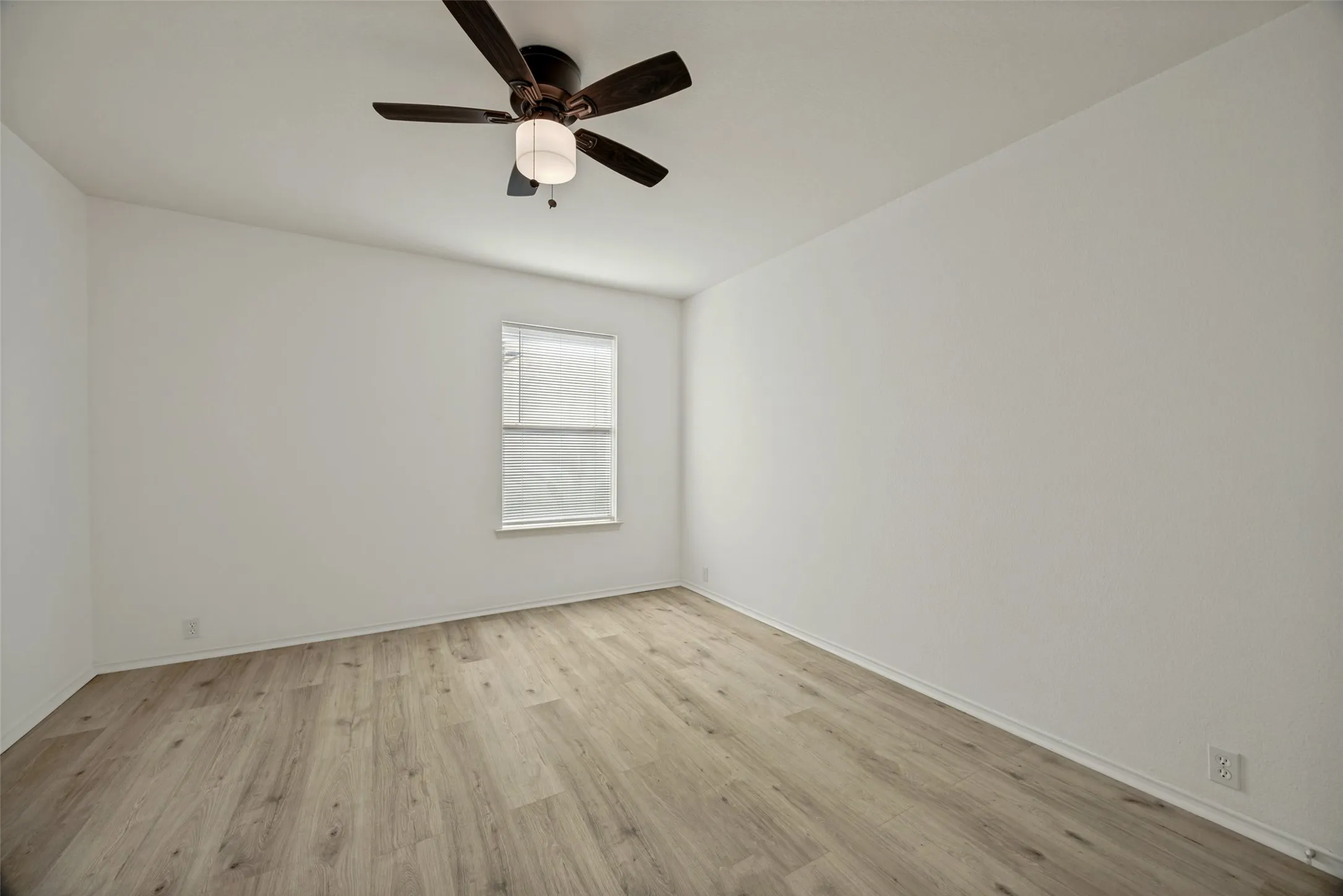 Light-filled room featuring wood-finish flooring, white walls, and a window with horizontal blinds