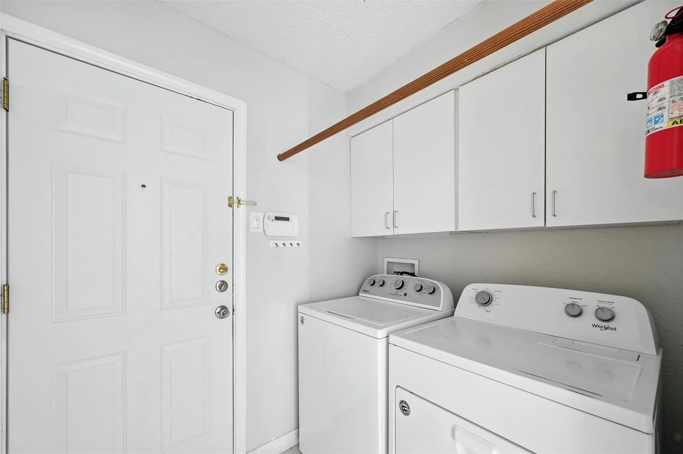 Dedicated laundry room featuring side-by-side washer and dryer units, white cabinetry with ample storage, neutral countertop workspace, and direct access to the home's exterior