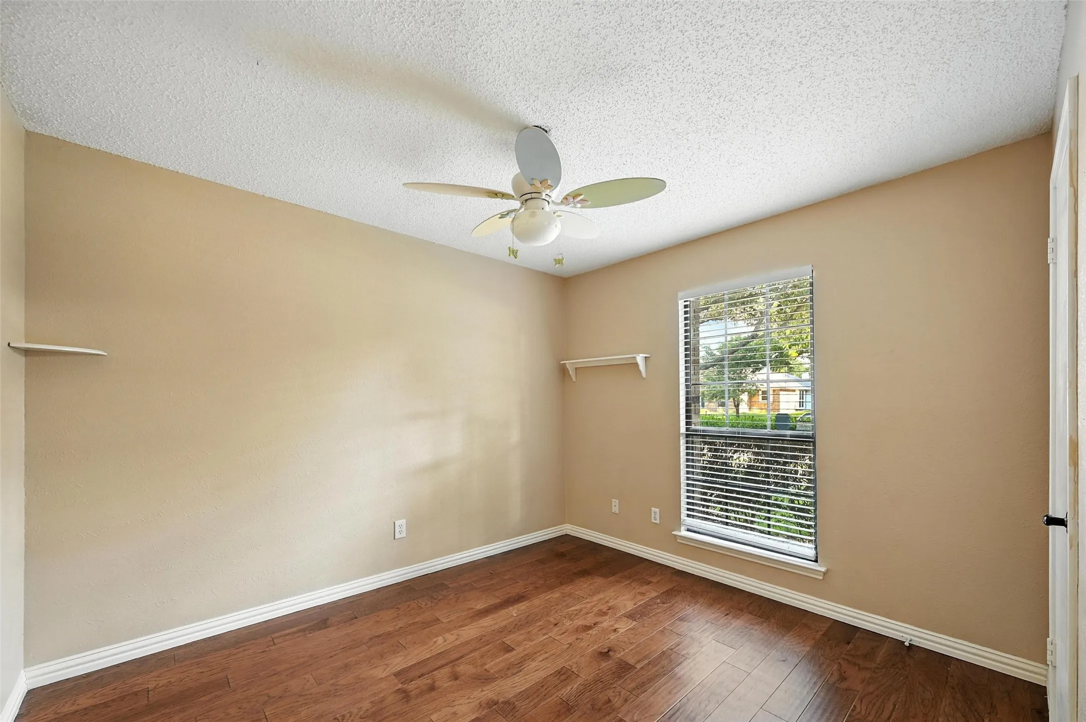 Bright corner bedroom with warm neutral walls, hardwood flooring, and ceiling fan with integrated lighting