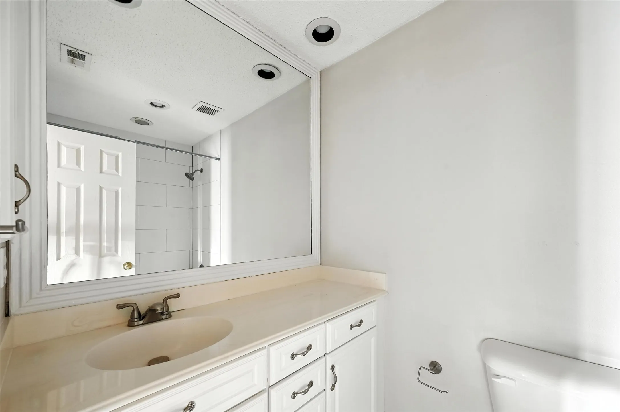 Elegant master bathroom featuring a generous wood-finish vanity with dual sink configuration, ample storage cabinetry with brushed nickel hardware, and a large framed mirror with integrated lighting
