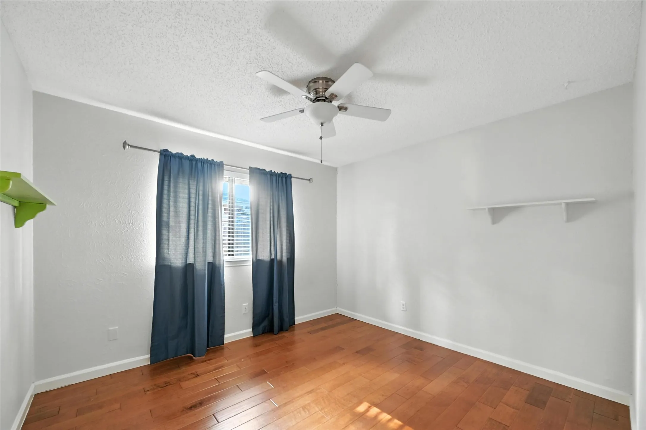 Spacious bedroom showcasing warm wood-finish flooring, ceiling fan with integrated lighting, and dual windows dressed in layered drapery that provide natural light and privacy control