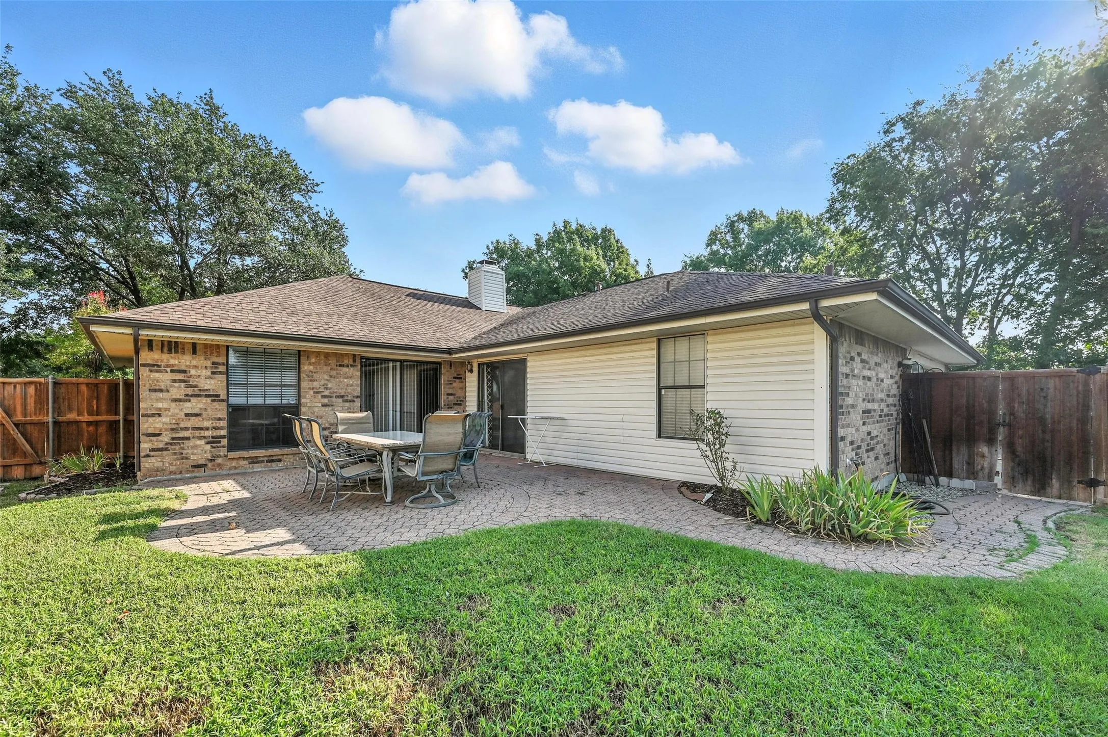 Charming single-story residence featuring a brick and siding exterior with a covered patio, mature landscaping with established trees, and a spacious manicured lawn