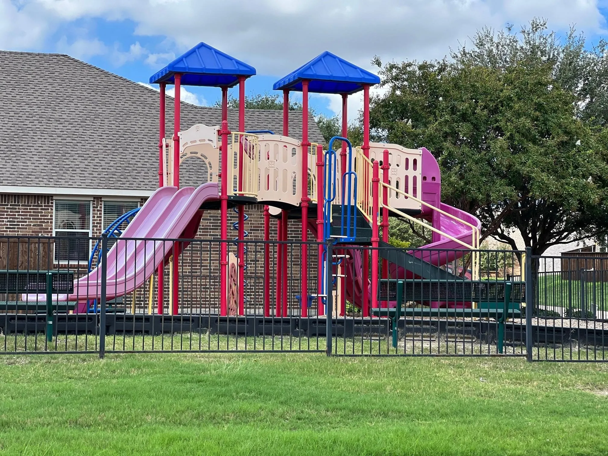 Community playground featuring multi-level play structures, multiple slides, shaded platforms, and ground-level fencing