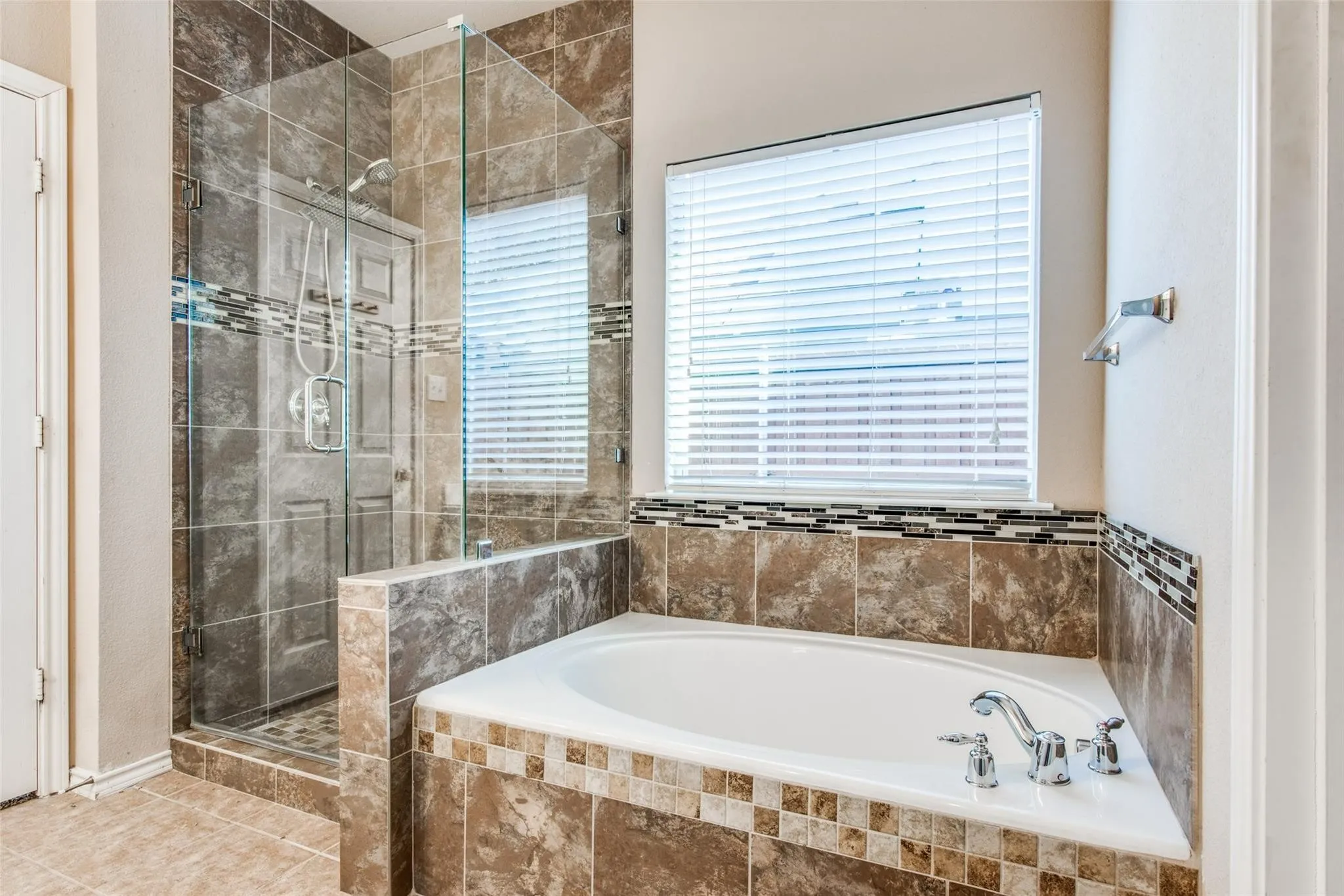 Soaking tub with chrome fixtures, surrounded by a tiled deck featuring decorative mosaic accents