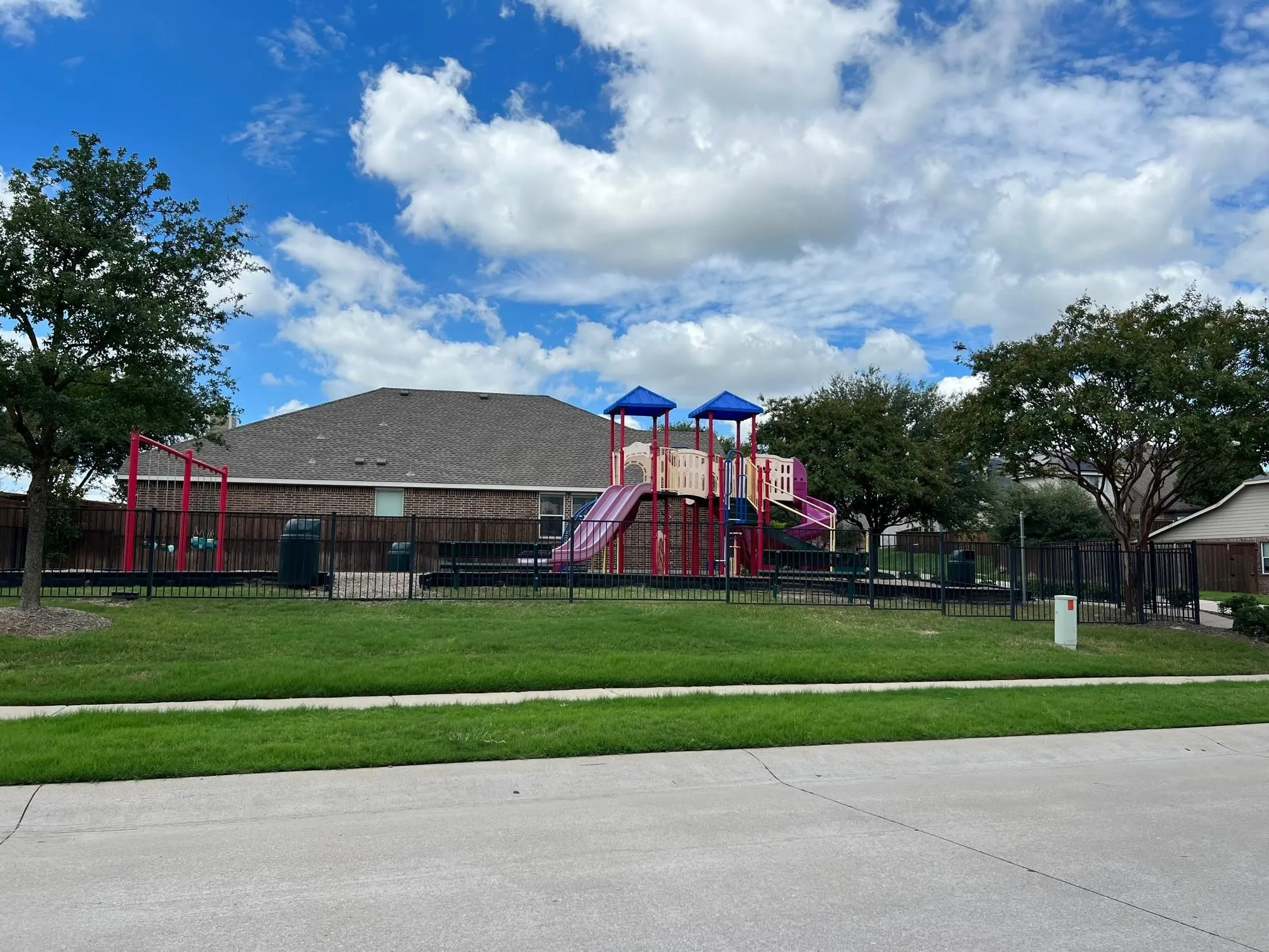 Community park featuring a play structure with slides and swings, surrounded by a black metal fence