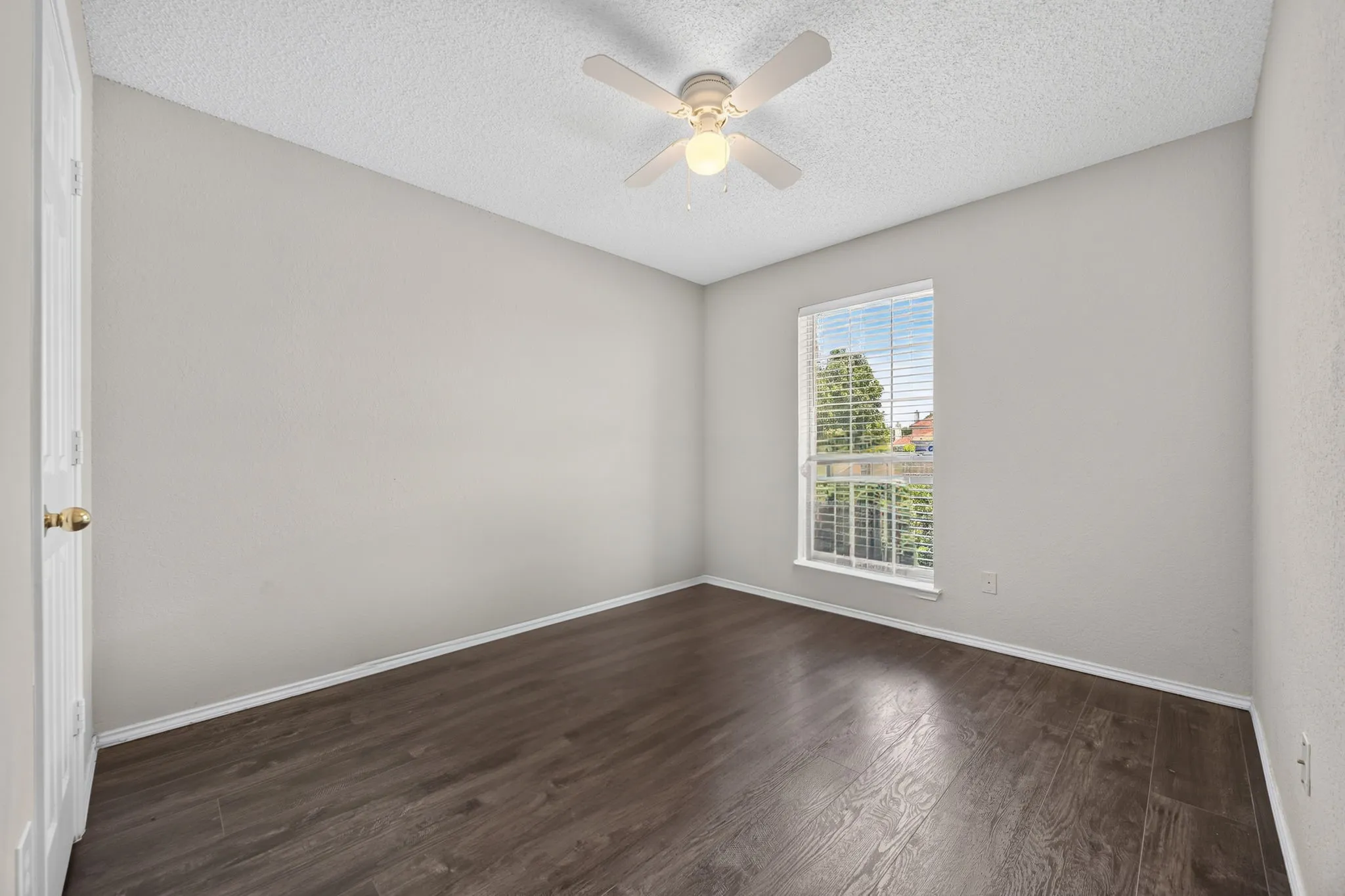 Spacious bedroom featuring dark wood-finish flooring, neutral wall finishes, and abundant natural light from a large window