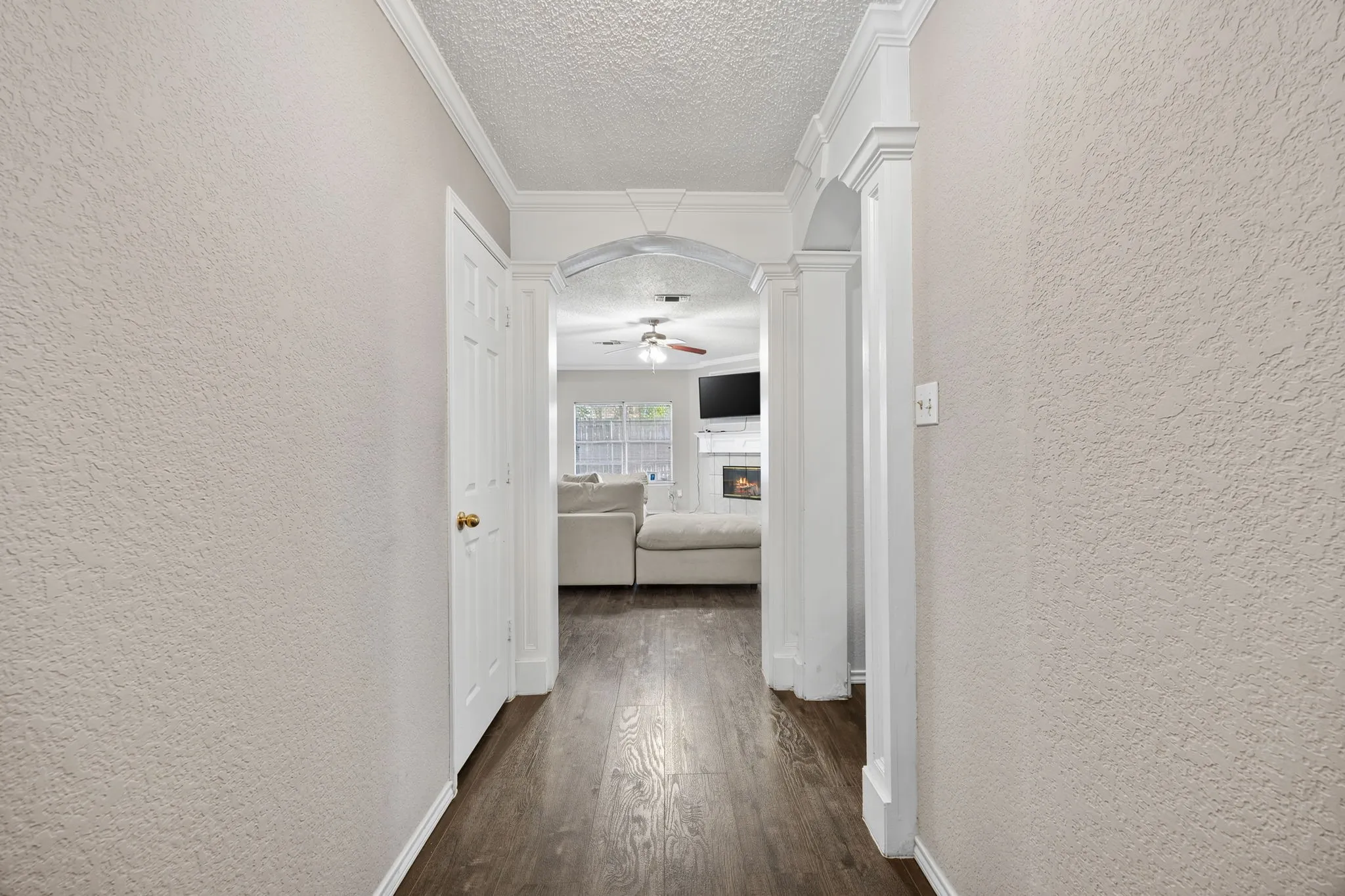Hallway with wood-finish flooring, textured walls, and crown molding