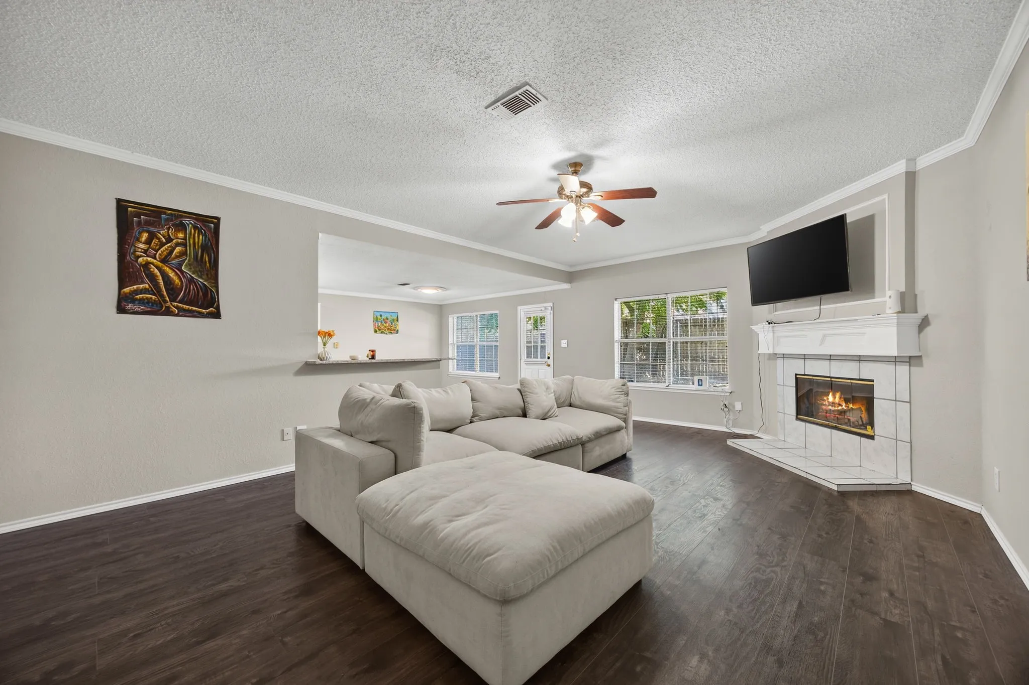 Spacious living room featuring a wood-finish plank floor, ceiling fan with integrated lighting, and a fireplace with white surround and built-in shelving
